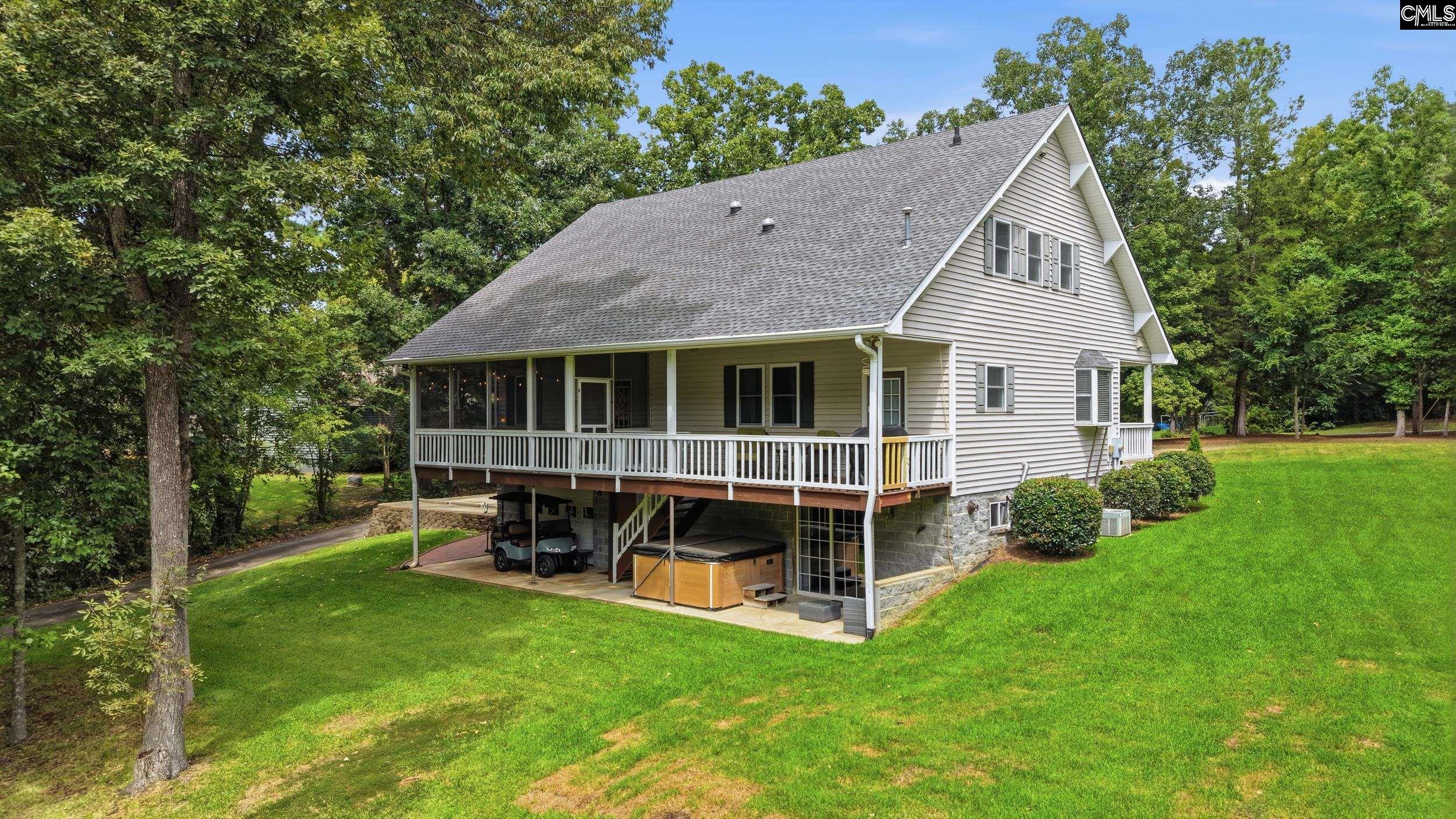 Home with a covered porch, raised lower level, carport, and hot tub beneath mature trees.