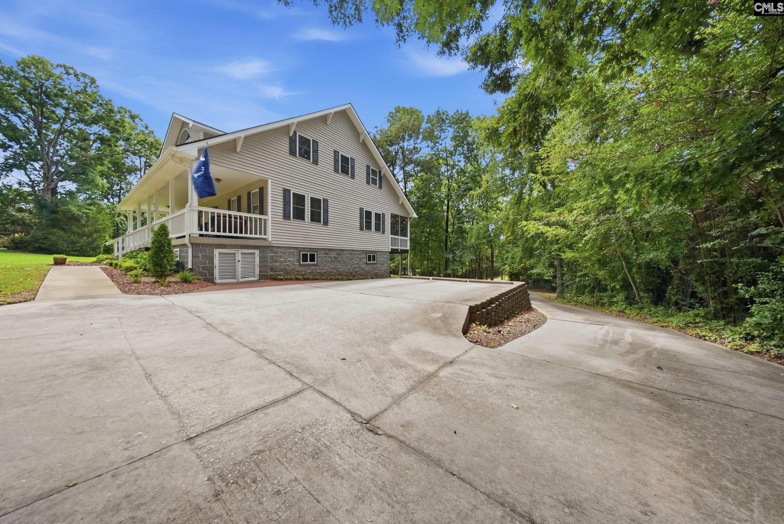 House with a covered porch and stone foundation beside a broad concrete driveway.