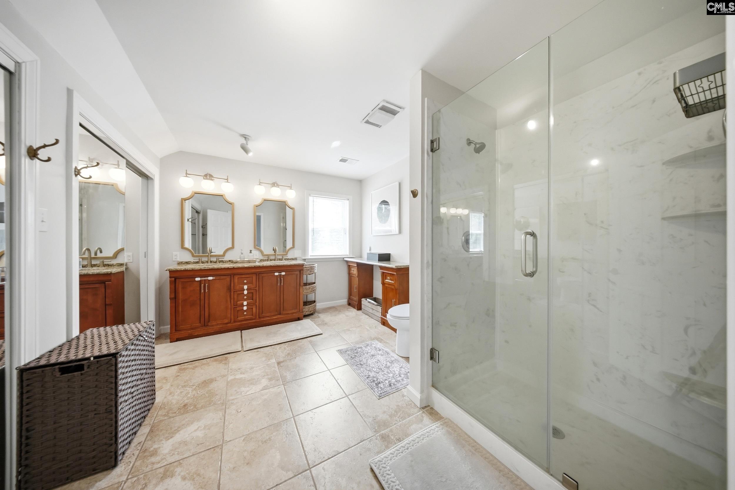 Spacious bathroom with a glass shower, double wood vanity, and large tiled floor.