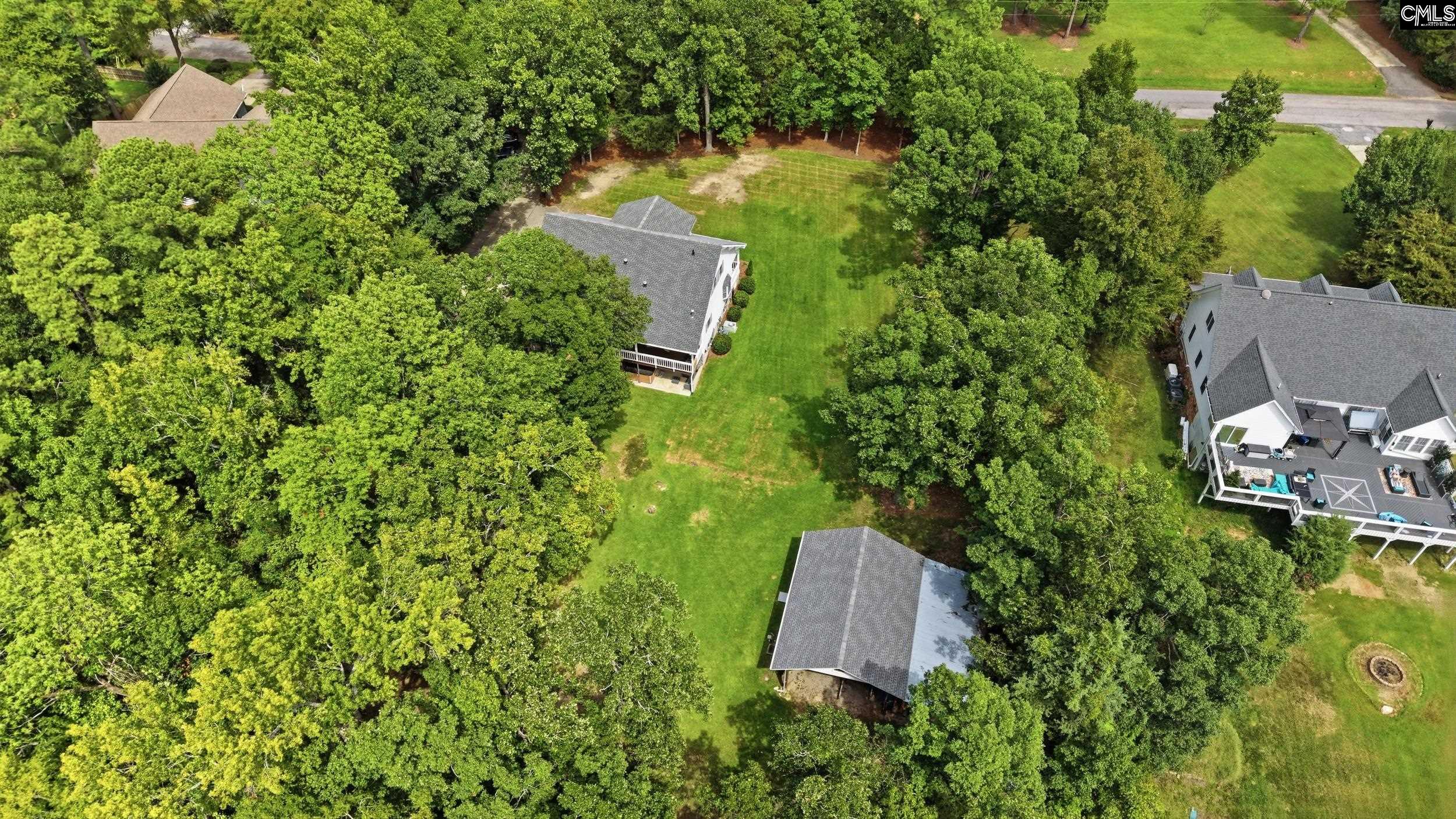 Aerial view of a home with a broad tree-lined lawn and detached outbuilding.