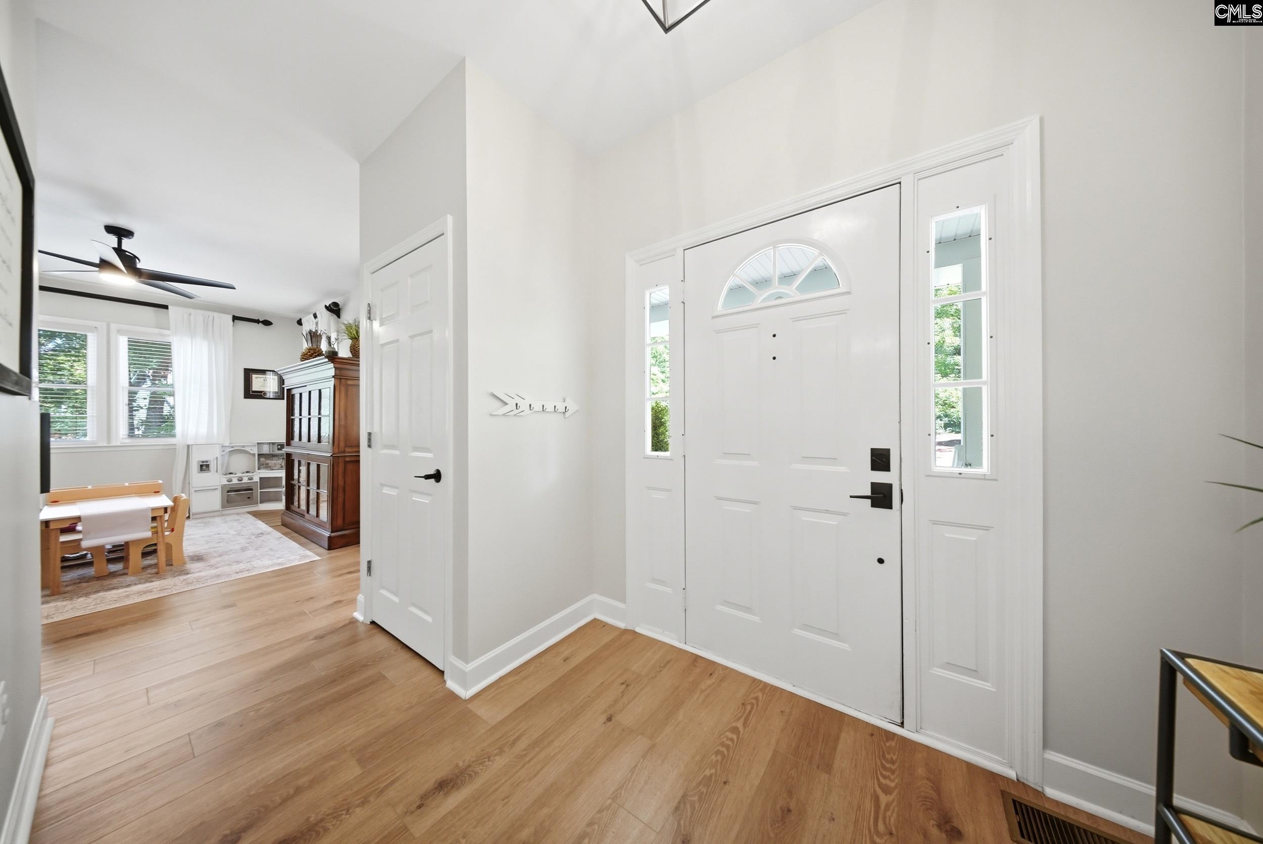 Entry foyer with a white front door, sidelights, light wood floors, and an adjoining playroom.