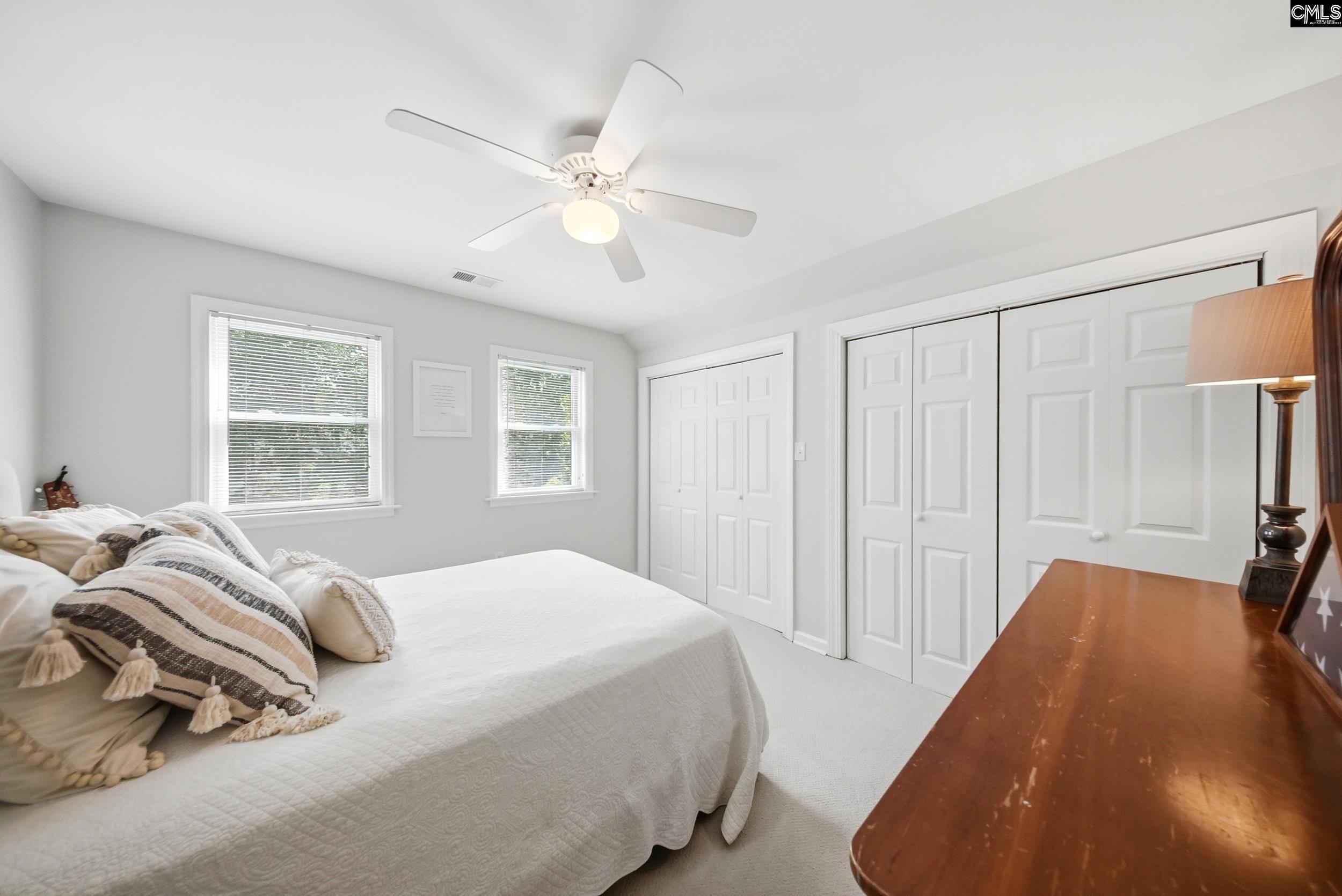 Bright bedroom with a white bed, ceiling fan, two windows, and double-door closets.