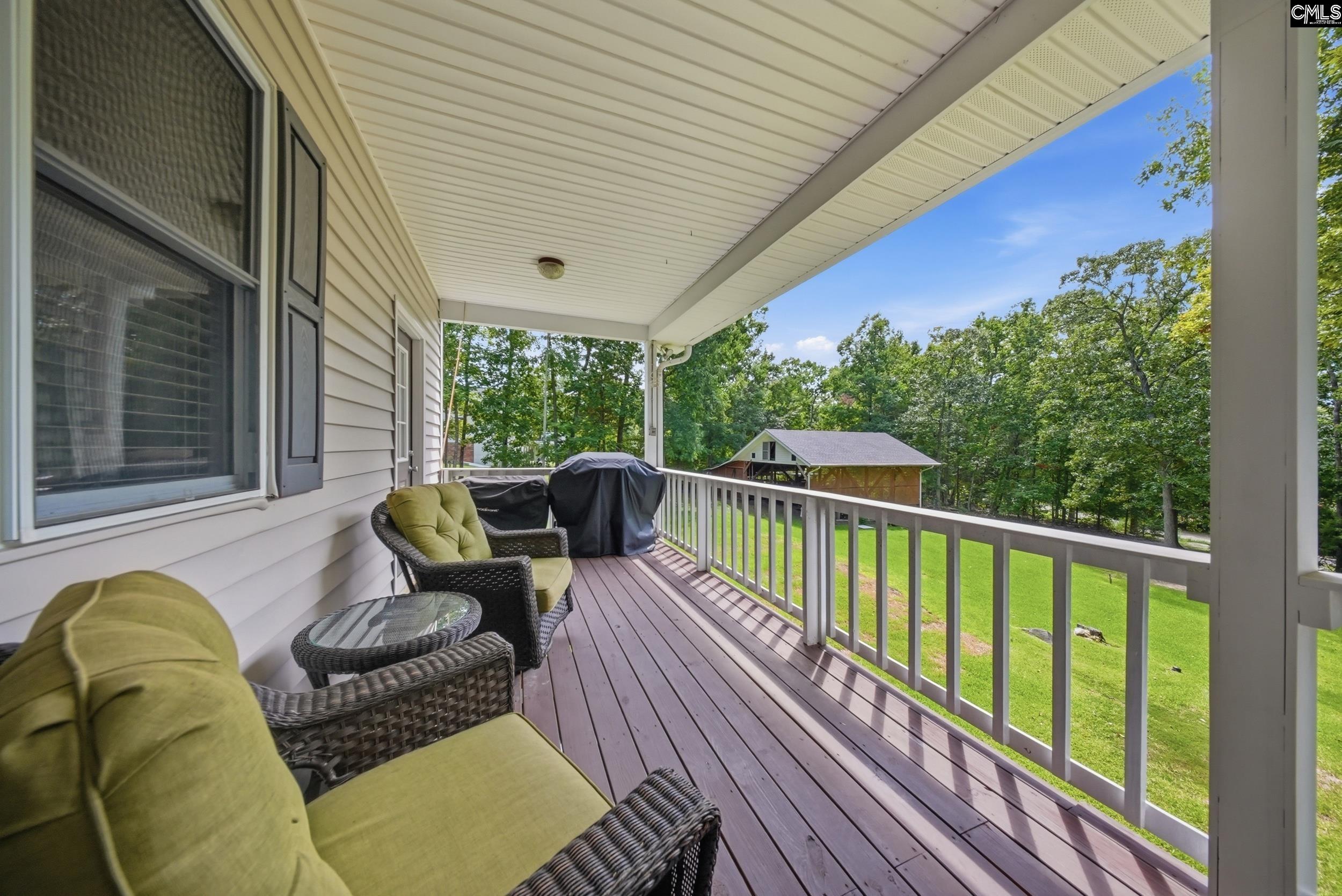 Covered porch with wicker seating overlooks a green lawn and wooded yard.