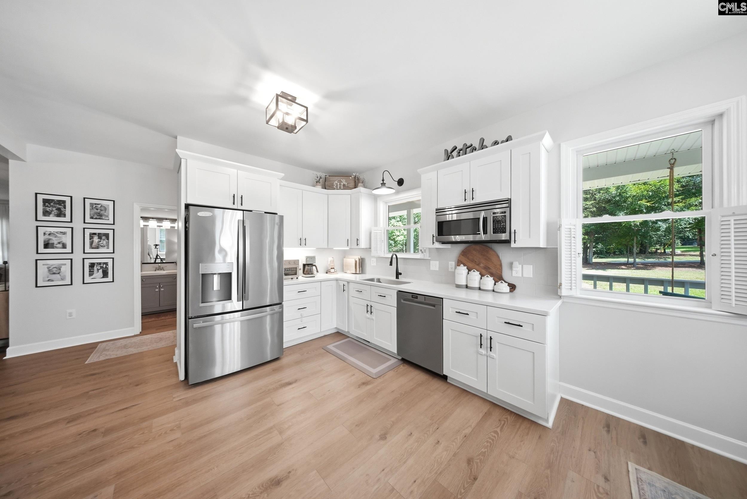 Bright kitchen with white cabinets, stainless steel appliances, and a large window overlooking trees.