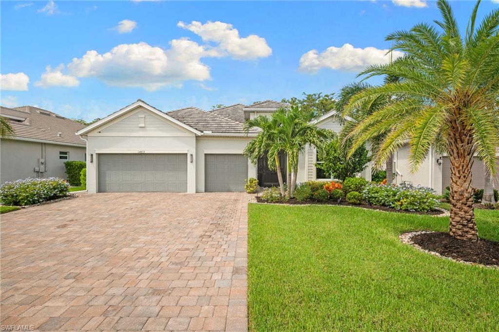 Single-story home with a three-car garage, paver driveway, lawn, and palm trees.