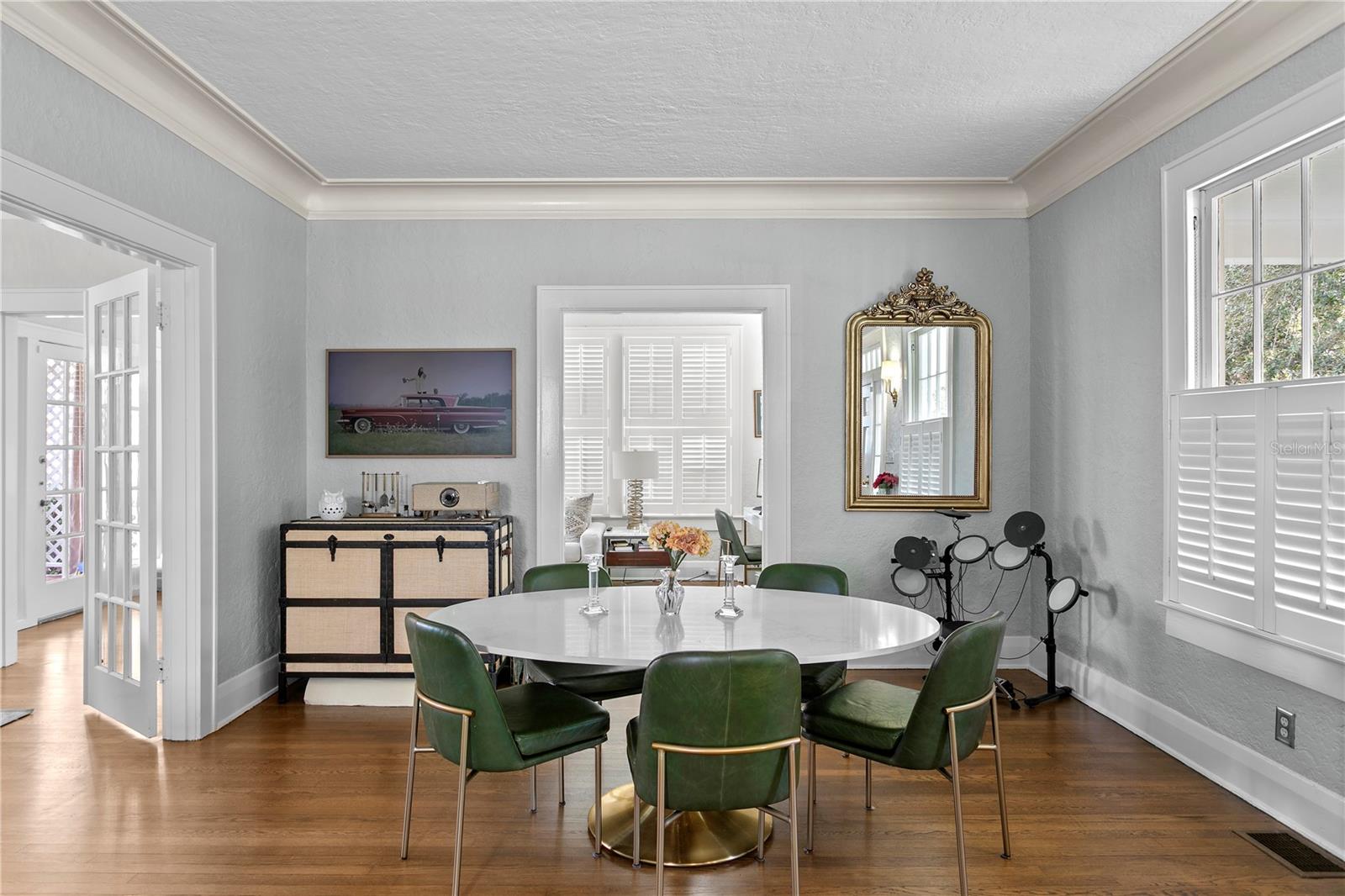 Dining room with a round white table, green leather chairs, and plantation-shuttered windows.