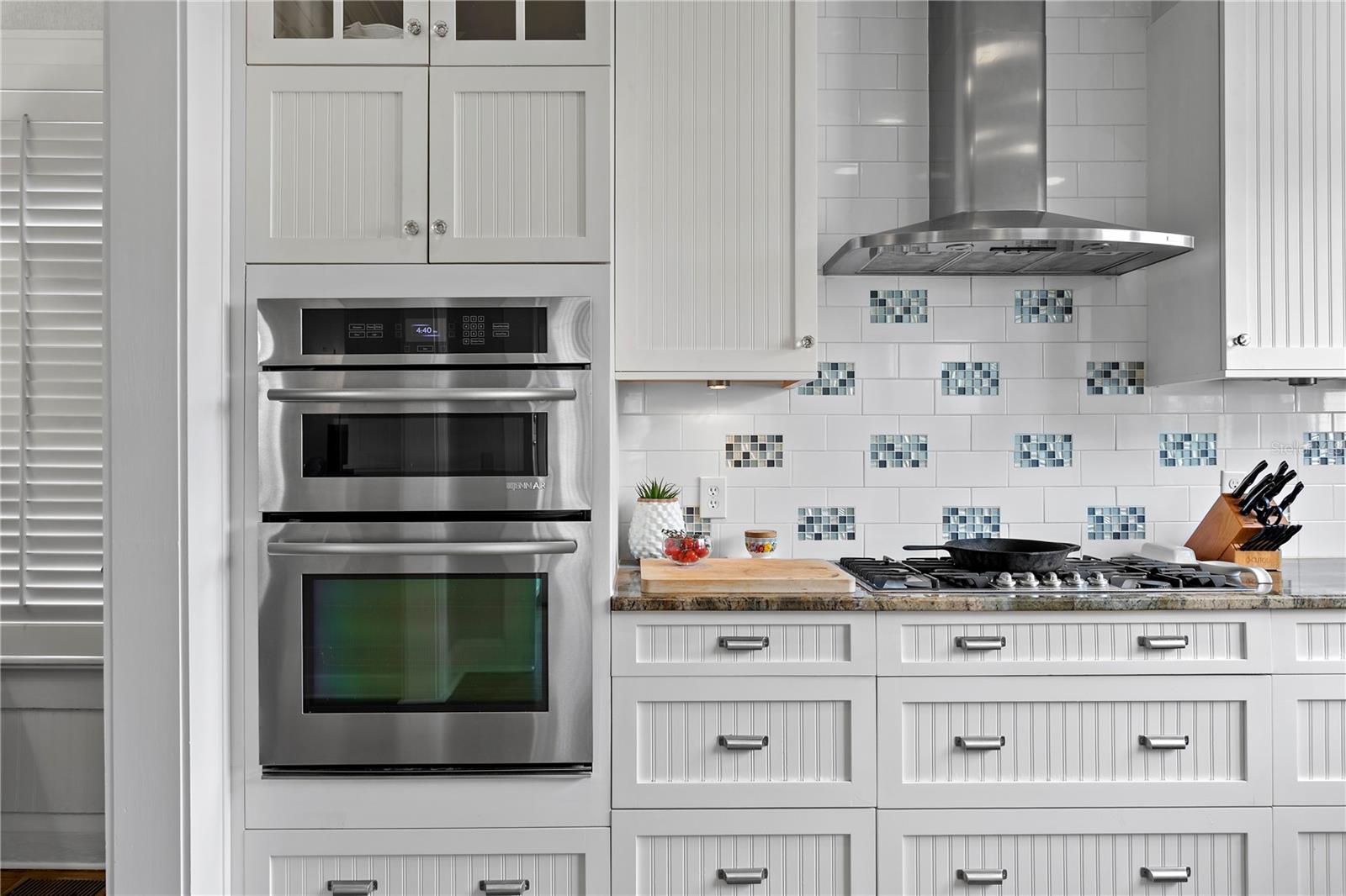 White kitchen with stainless double ovens, gas cooktop, and blue-accented tile backsplash.