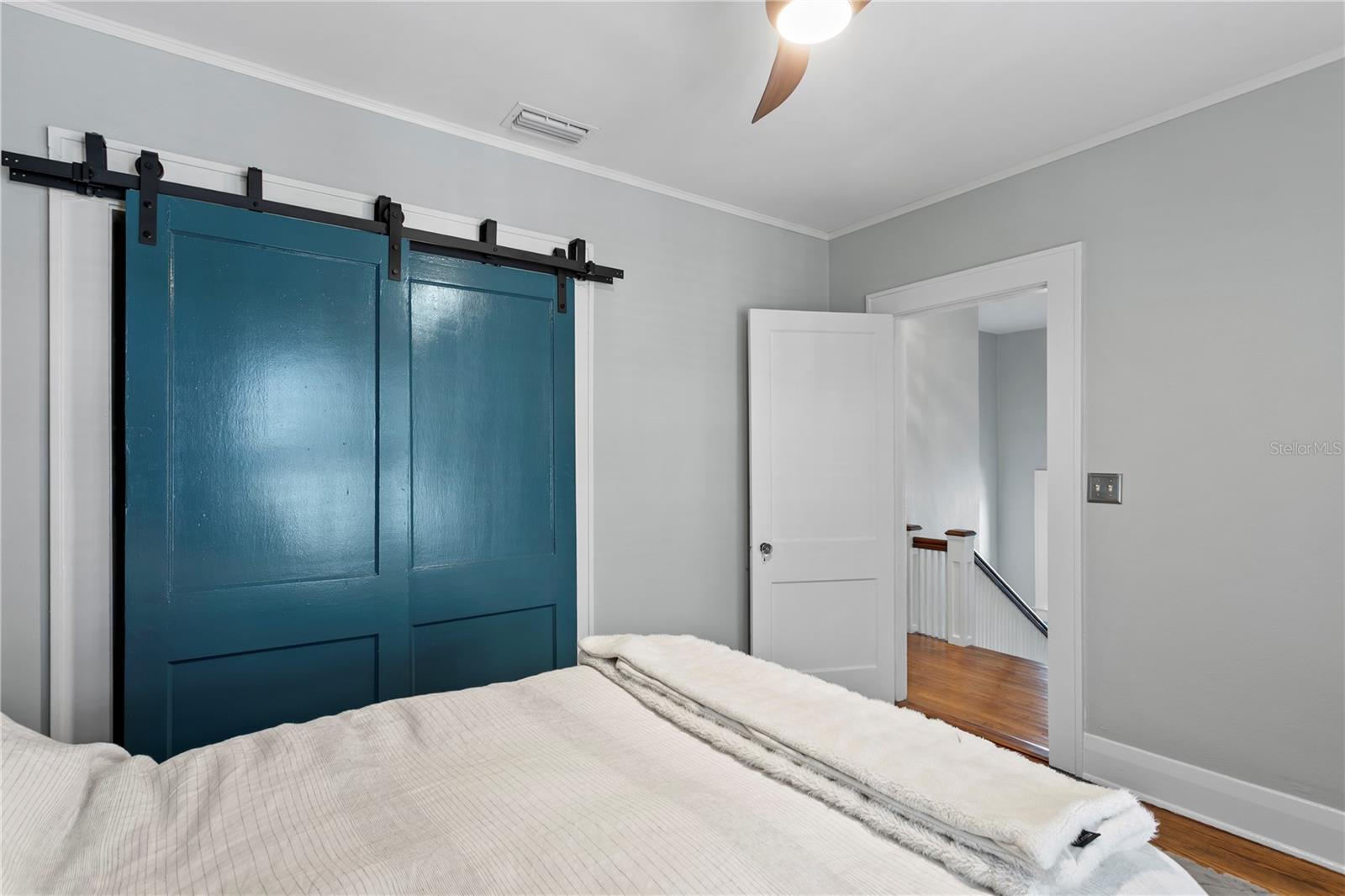 Bedroom with teal sliding barn doors and an open doorway to a hardwood landing.