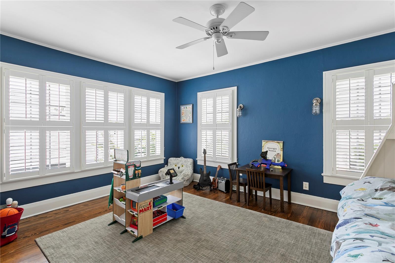 Bedroom with blue walls, plantation shutters, a child-sized market stand, guitars, and a bed.