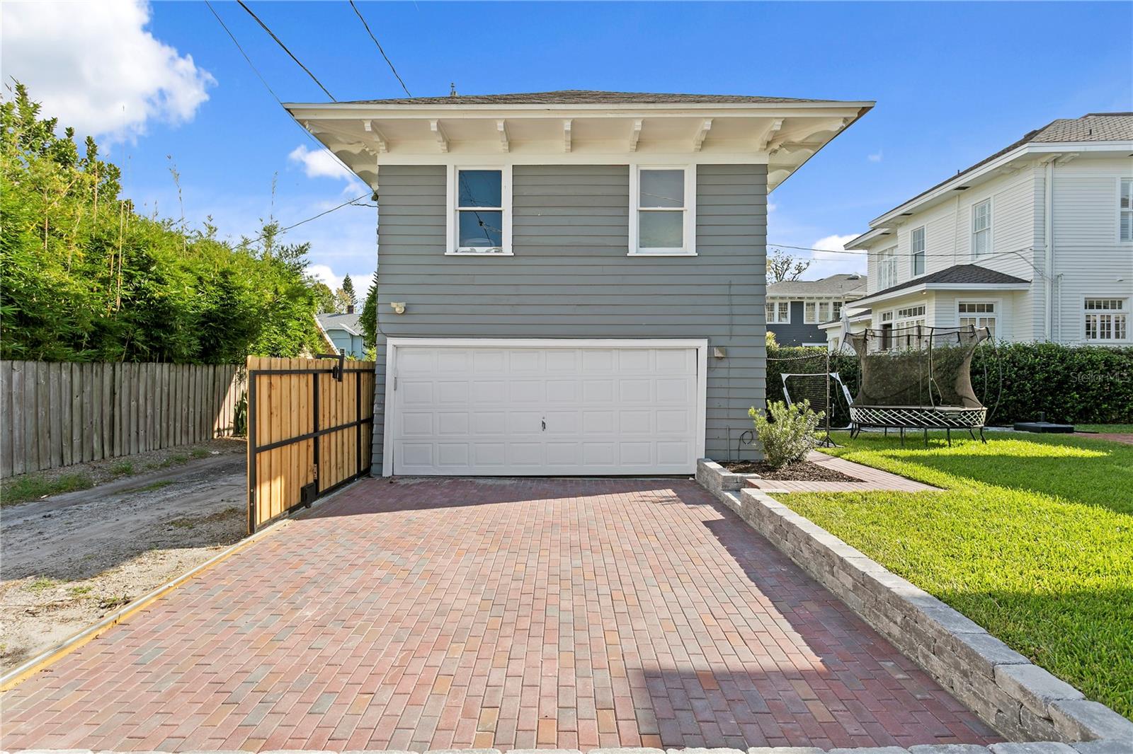 Gray two-story garage with a white double door and wide brick-paver driveway.