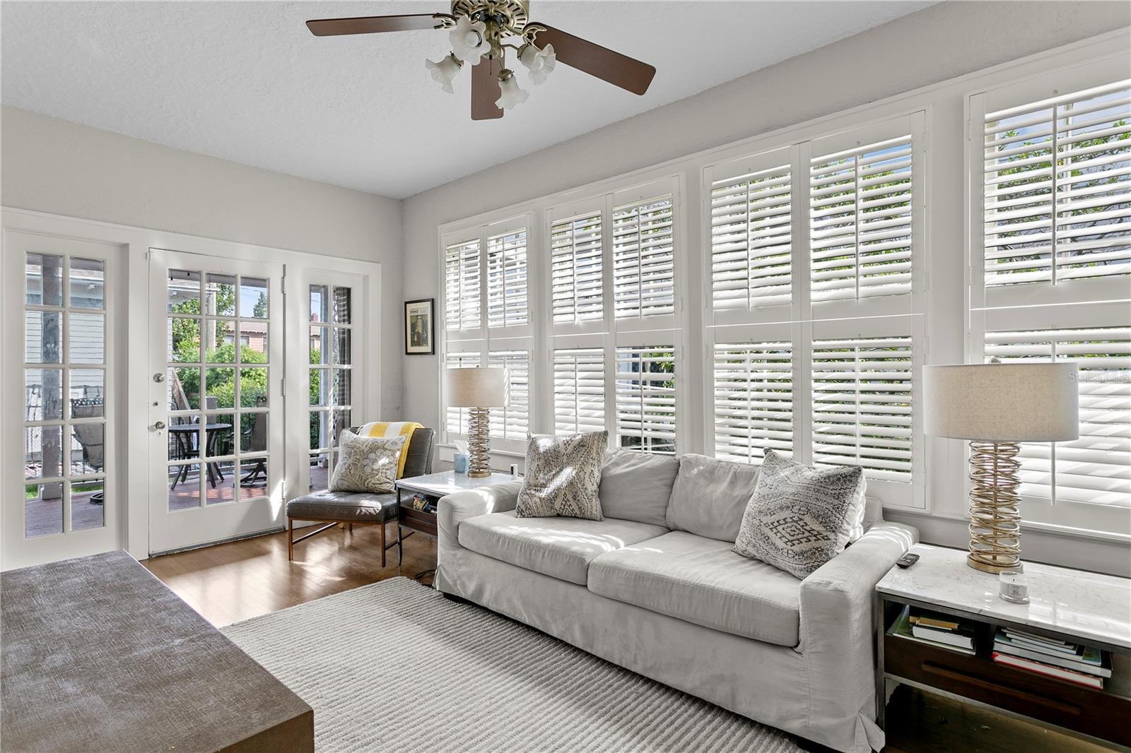 Living room with plantation shutters, a white sofa, and French doors opening to a patio.