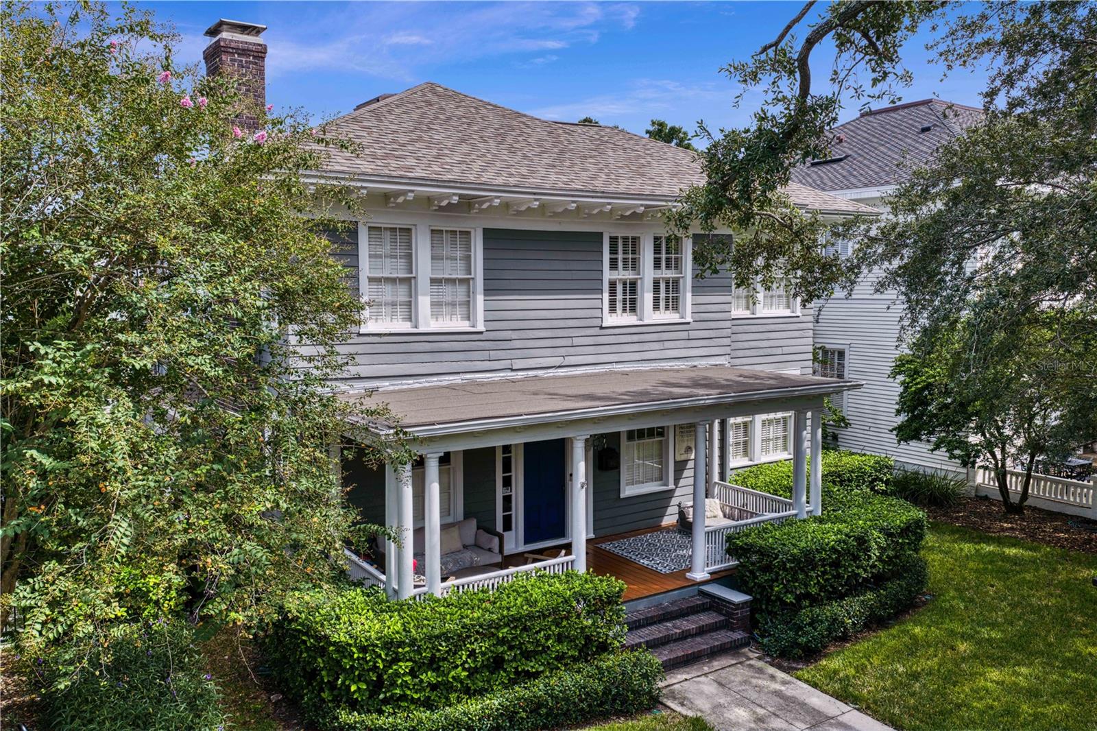 Two-story gray house with a covered porch, blue front door, and hedges along the walkway.