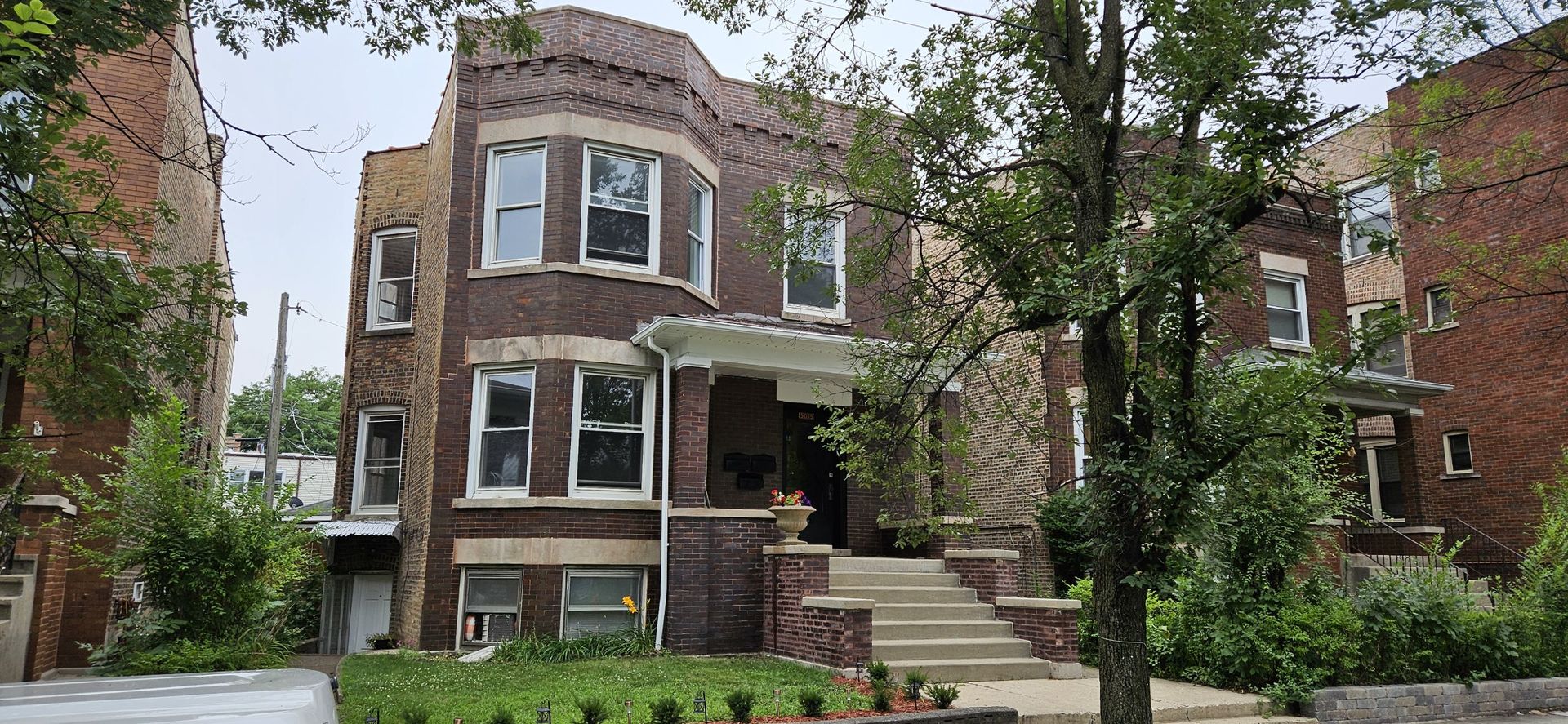 Brick apartment building with projecting bay windows, broad front steps, and mature trees.