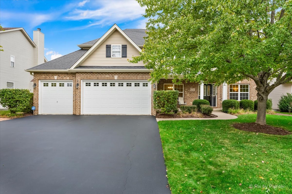 Two-story brick-and-siding home with a double garage, broad driveway, and leafy tree over the lawn.