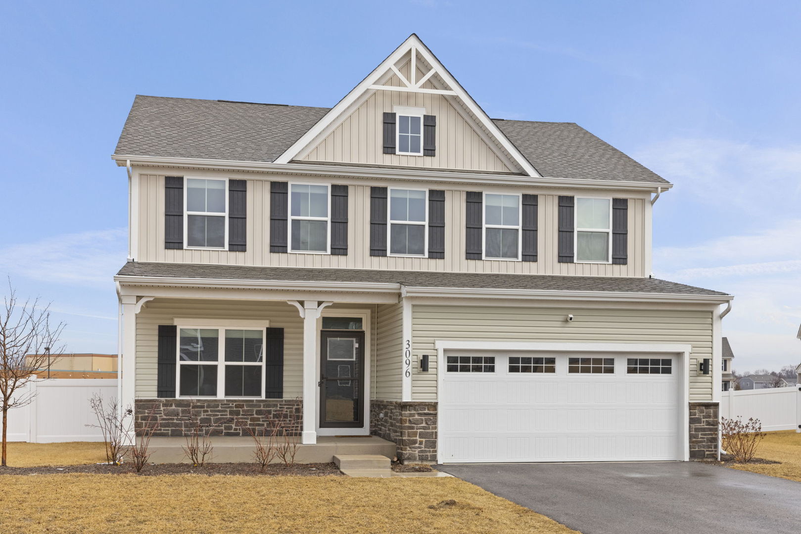 Two-story beige house with a steep gable, stone foundation, covered porch, and attached white garage.