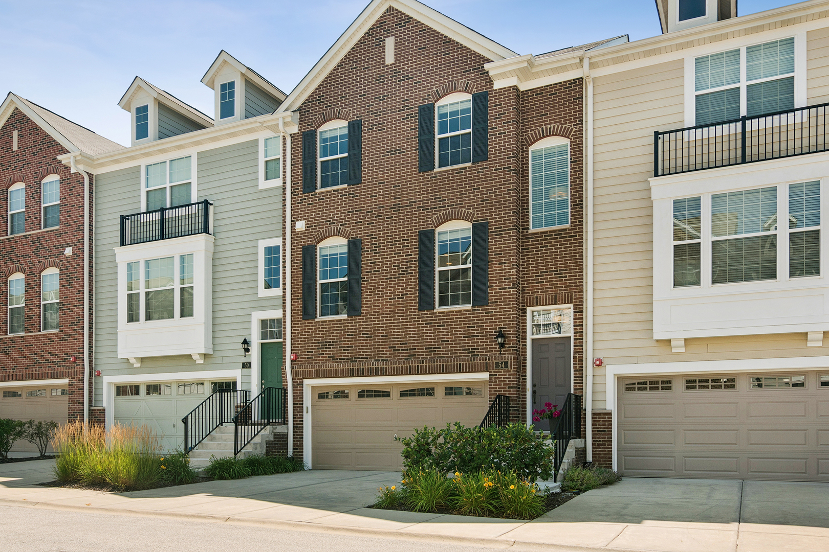 Three-story brick townhouse marked 54, with a two-car garage, black shutters, and landscaped entry.