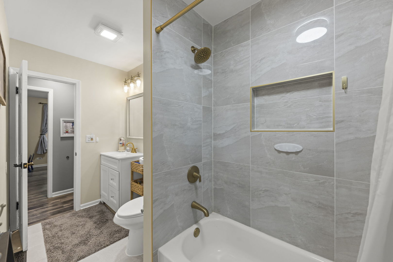 Bathroom with a gray tiled tub and shower, gold fixtures, and a recessed niche.