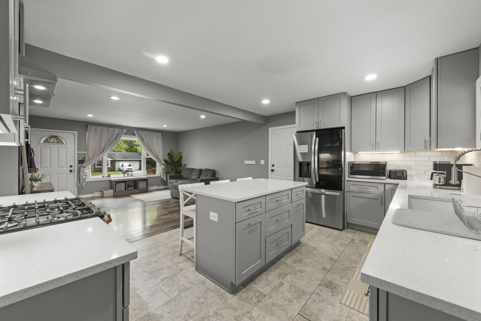 Open-plan kitchen with gray cabinets, stainless steel appliances, and a large island beside the living area.