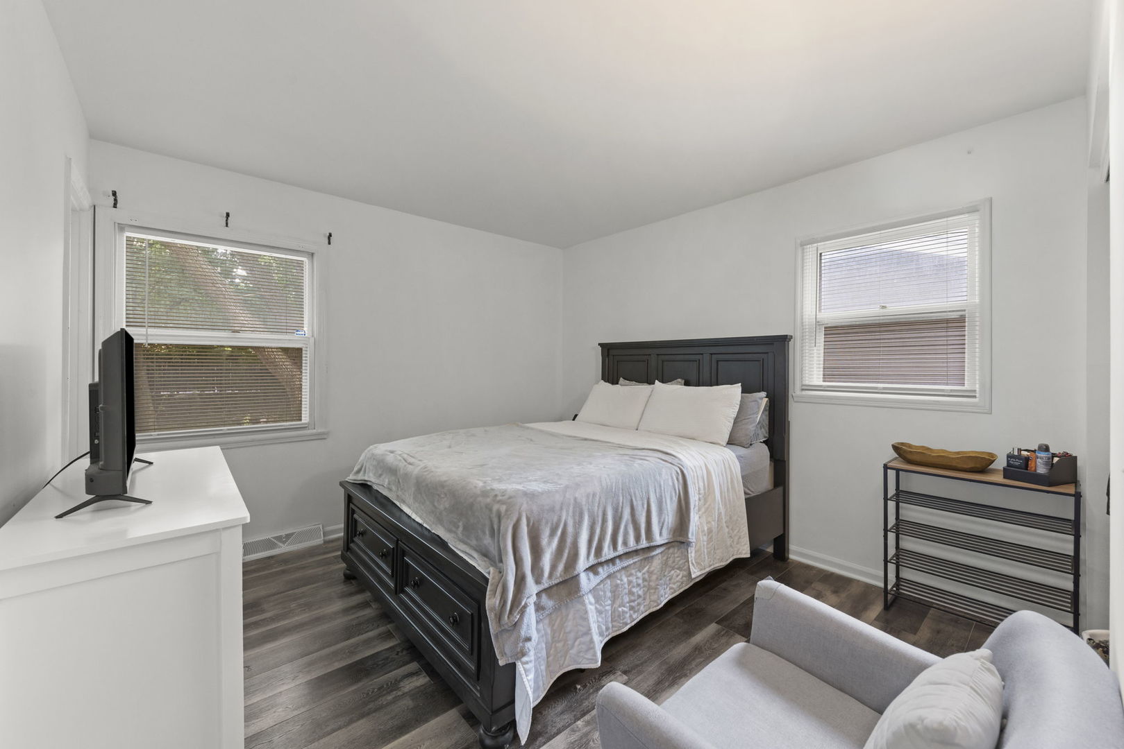 Bedroom with a dark wood bed, gray flooring, and windows with blinds.
