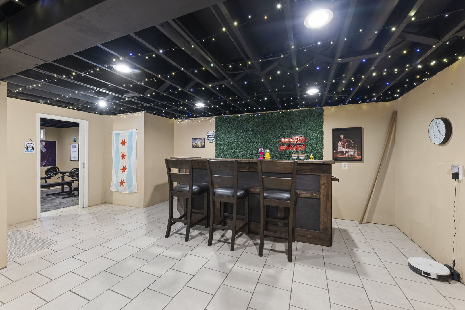 Finished basement bar with four stools, a green foliage wall, and a ceiling of twinkling lights.