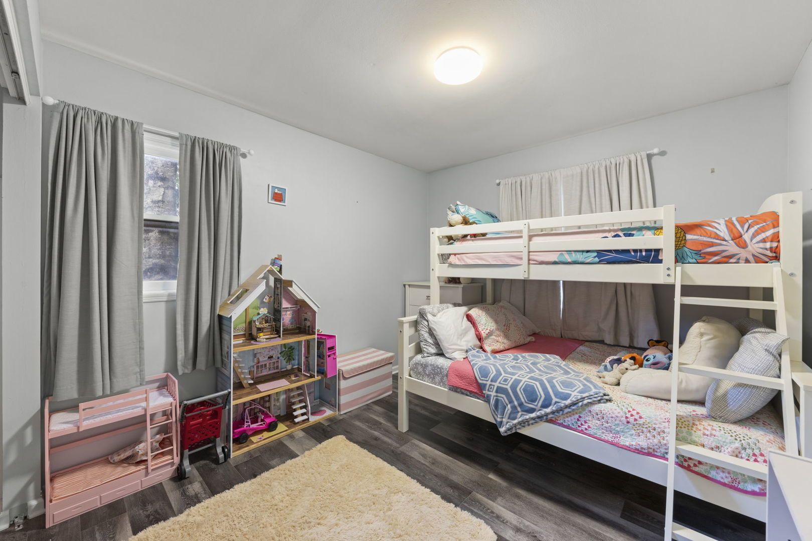 Children’s bedroom with a white bunk bed, colorful bedding, dollhouse, and toy beds.