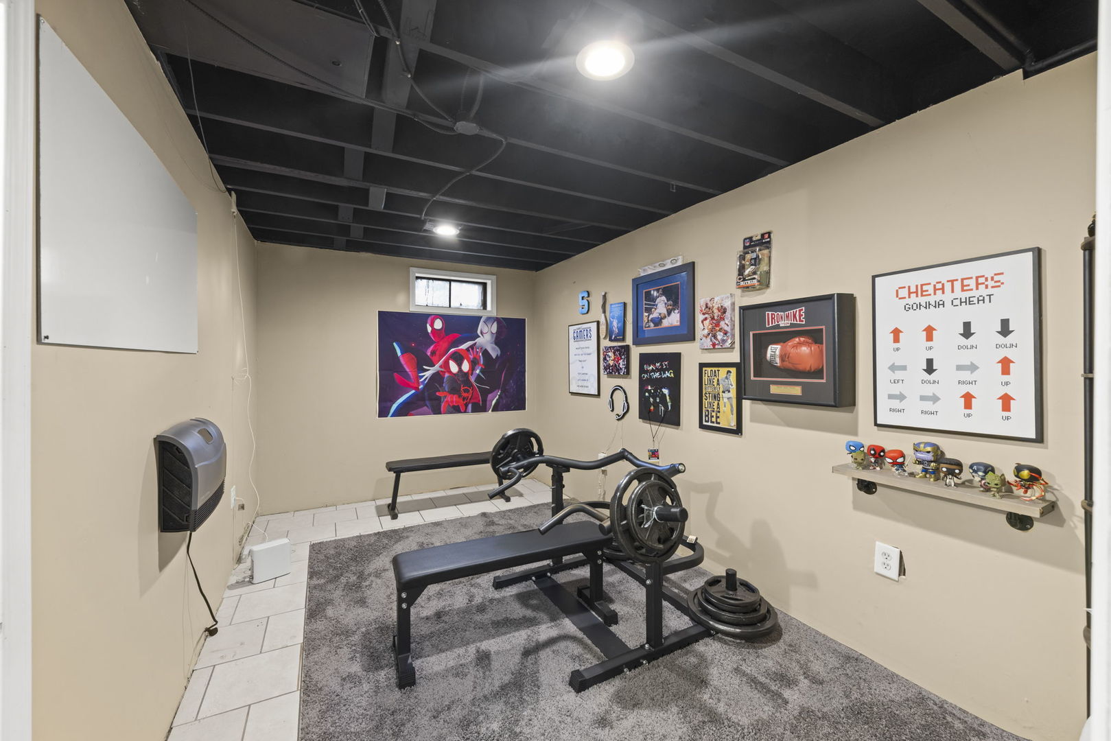 Home gym with a weight bench, barbell, and sports and superhero memorabilia on the walls.