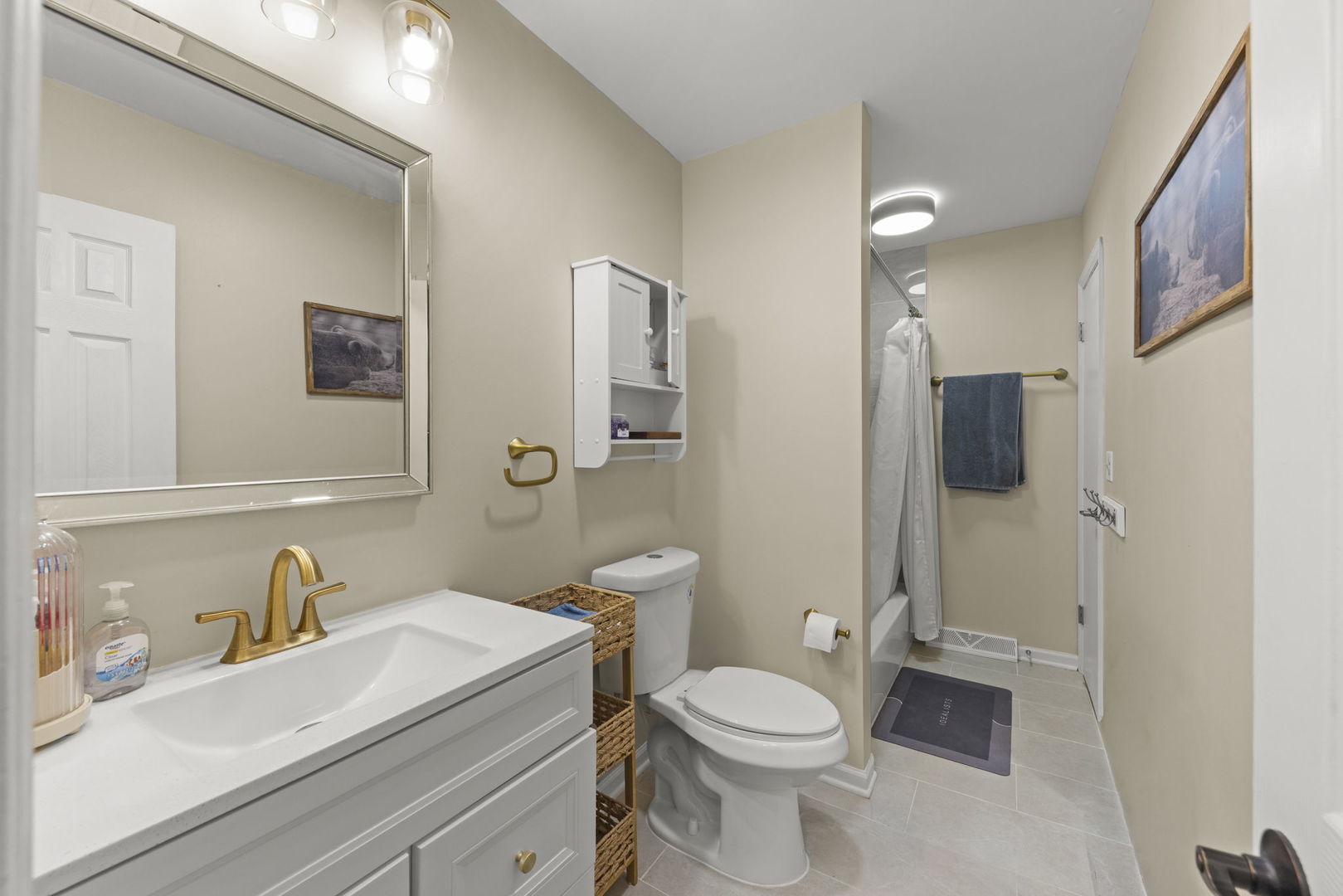 Bathroom with a white vanity, gold faucet, large mirror, and shower at the far end.