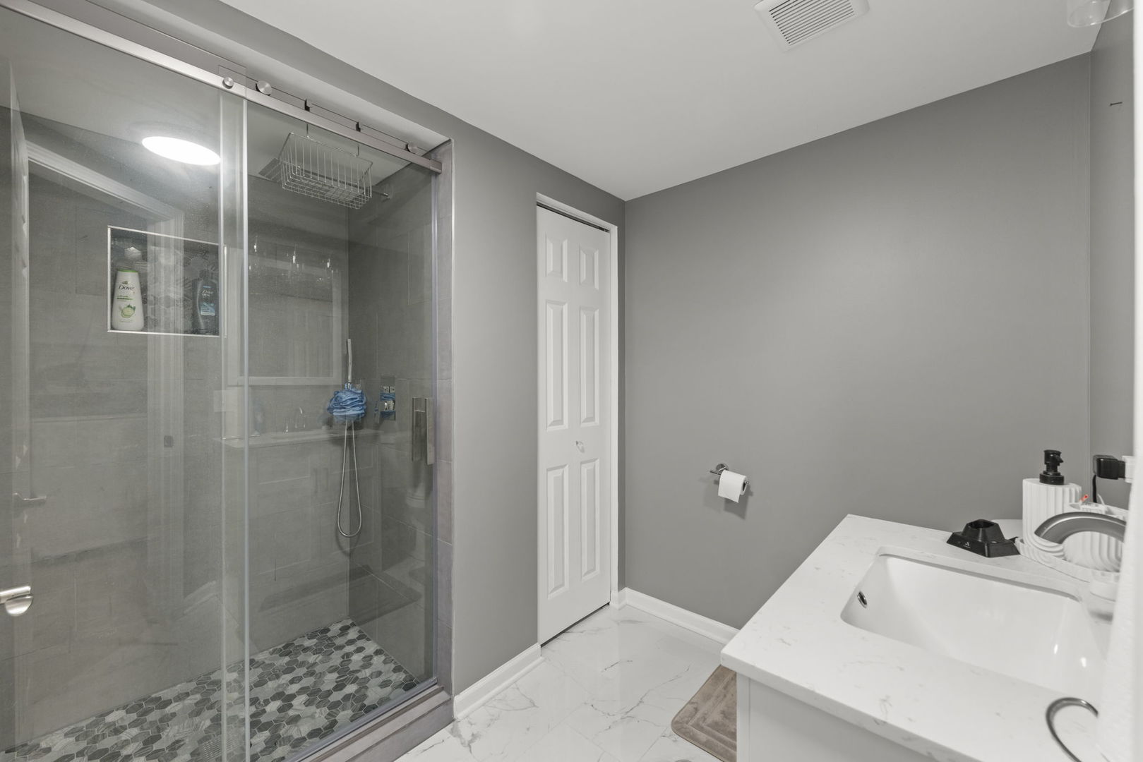 Bathroom with a glass-enclosed shower, pebble mosaic floor, and white marble-look vanity.