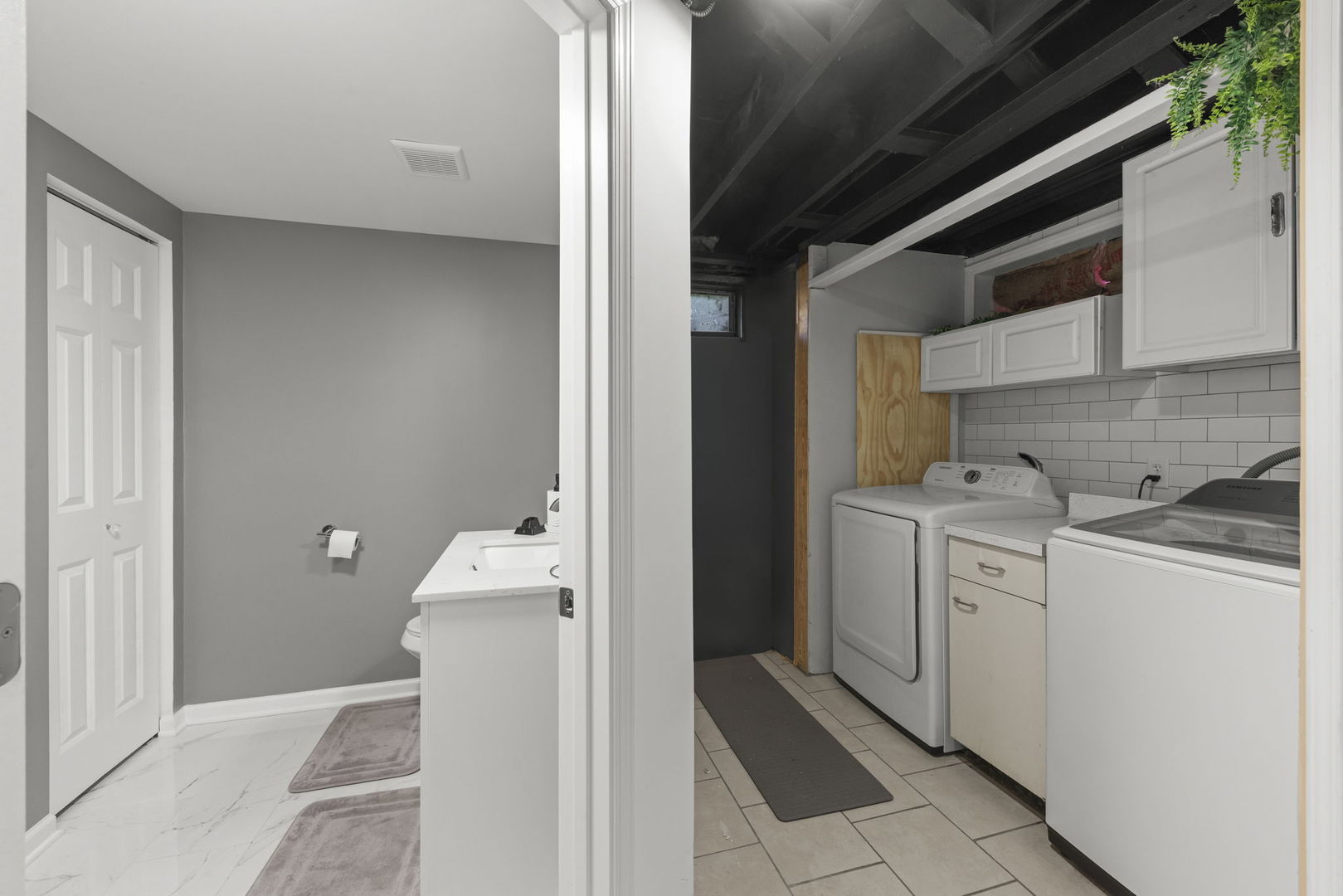 Basement laundry room with white cabinets and subway tile beside a gray bathroom.