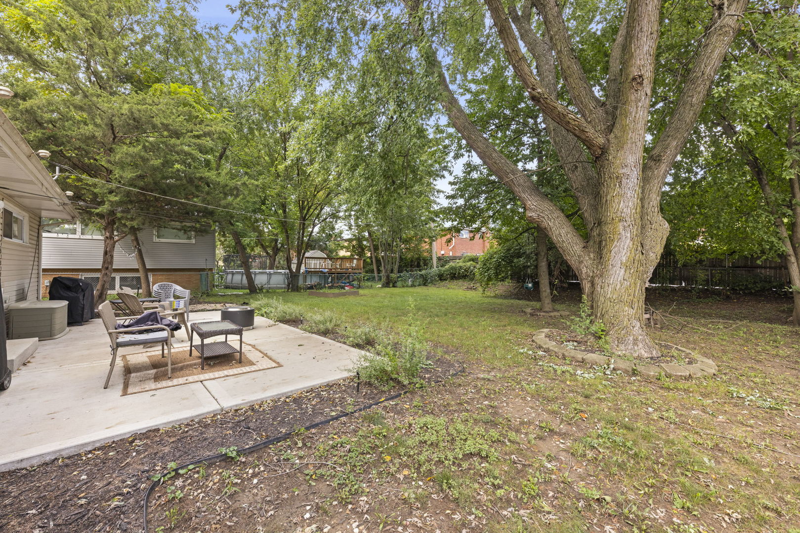 Backyard patio with outdoor seating beneath mature shade trees.