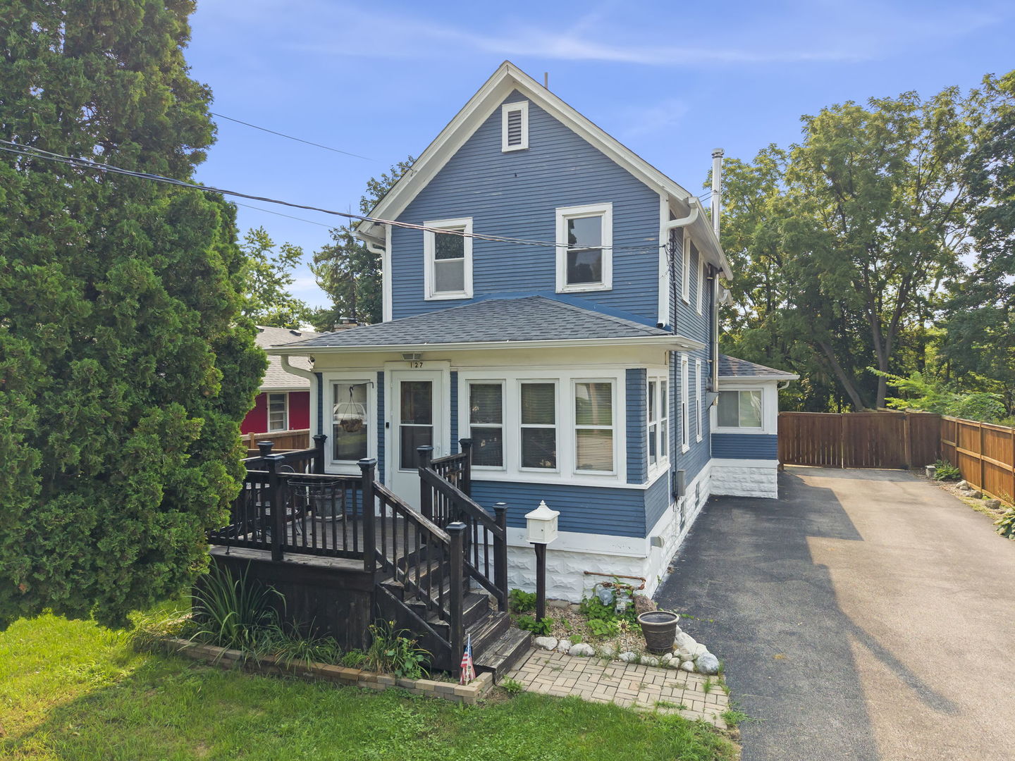 Blue two-story house with white trim, a raised wooden deck, and a paved driveway.