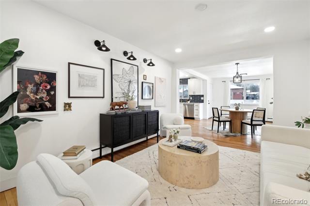 Living room with white seating and a round stone coffee table, opening to the dining area and kitchen.