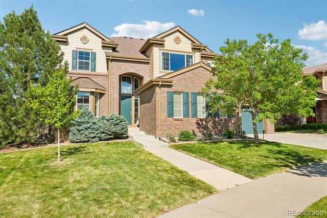 Two-story brick-and-siding home with teal shutters, a front lawn, mature trees, and a concrete walkway.