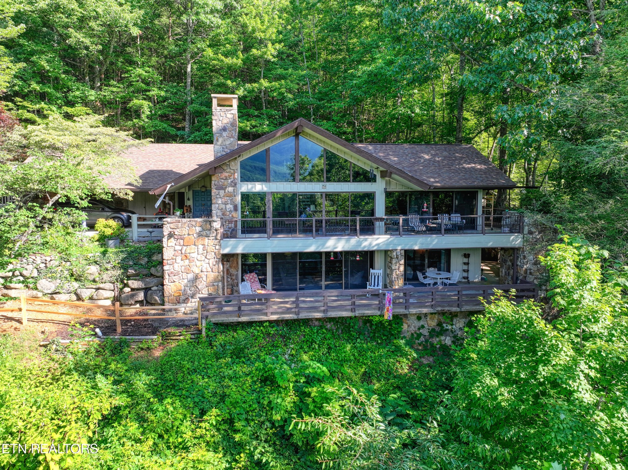 Wooded home with a stone chimney, tall glass gable, and two spacious decks.