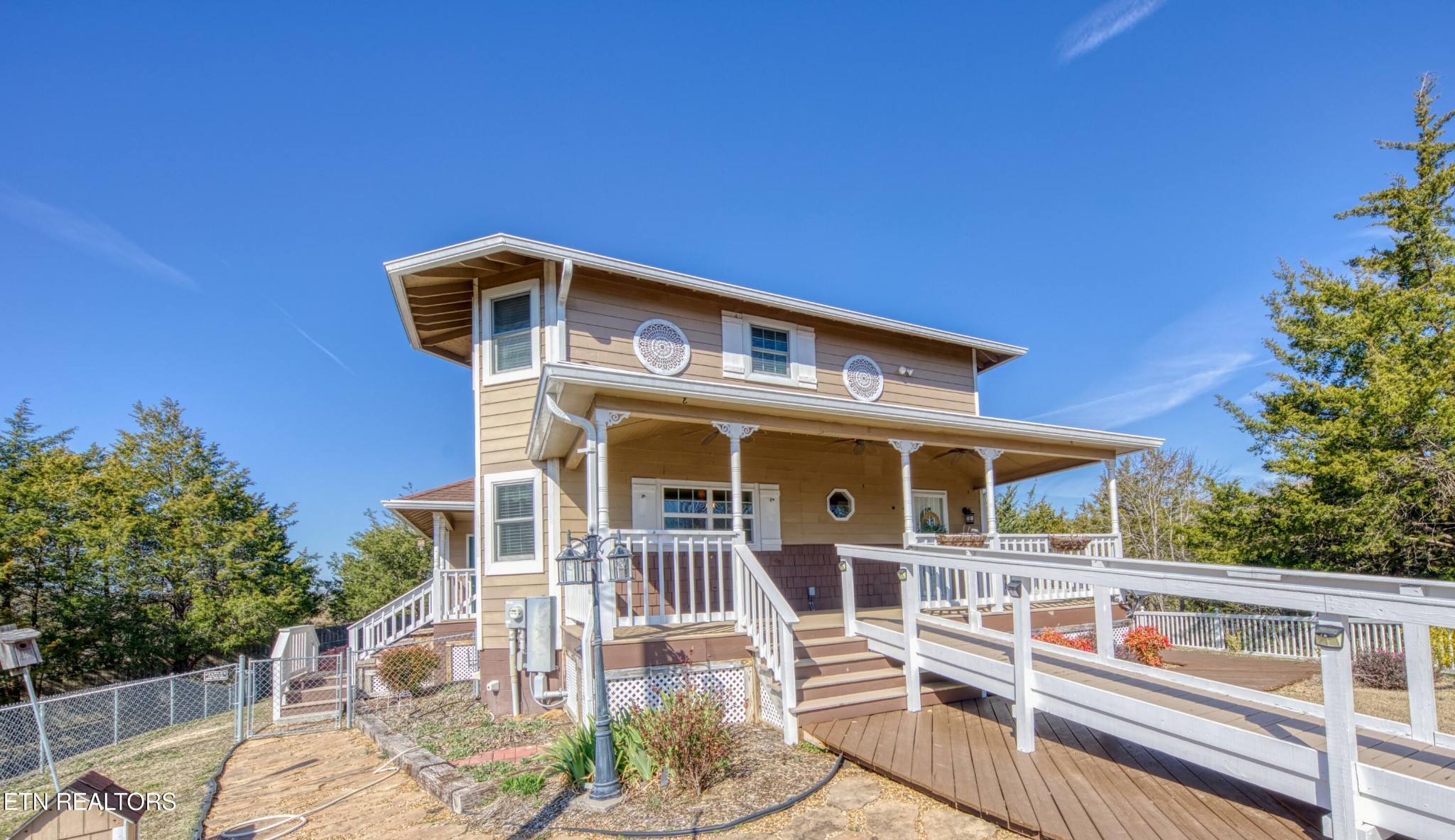 Tan two-story house with a covered porch and a long white-railed accessibility ramp.