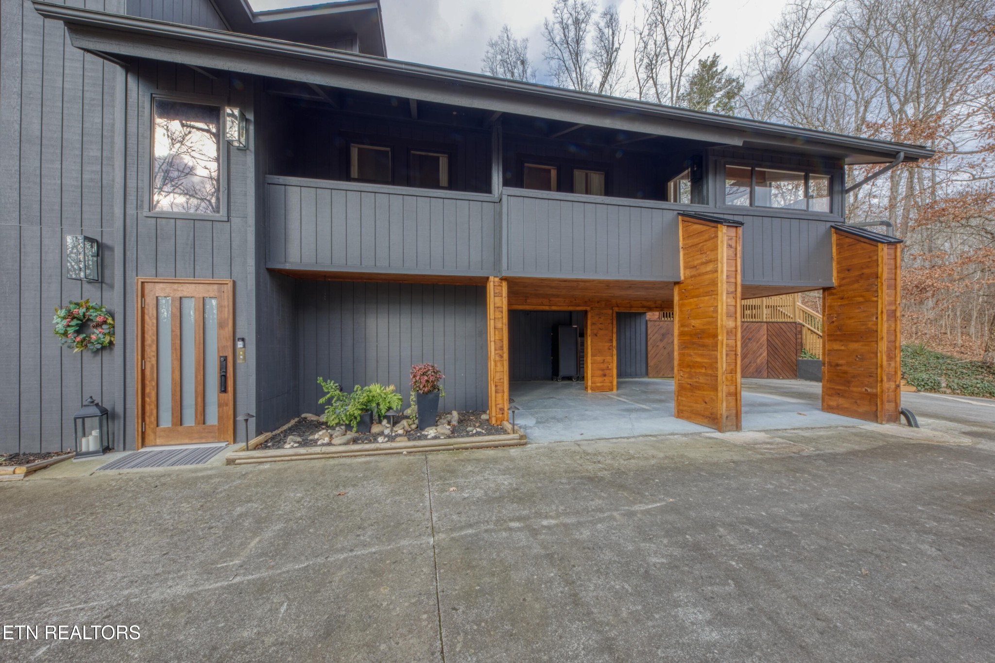 Modern gray home with a wood-framed glass entry and a covered driveway supported by timber posts.