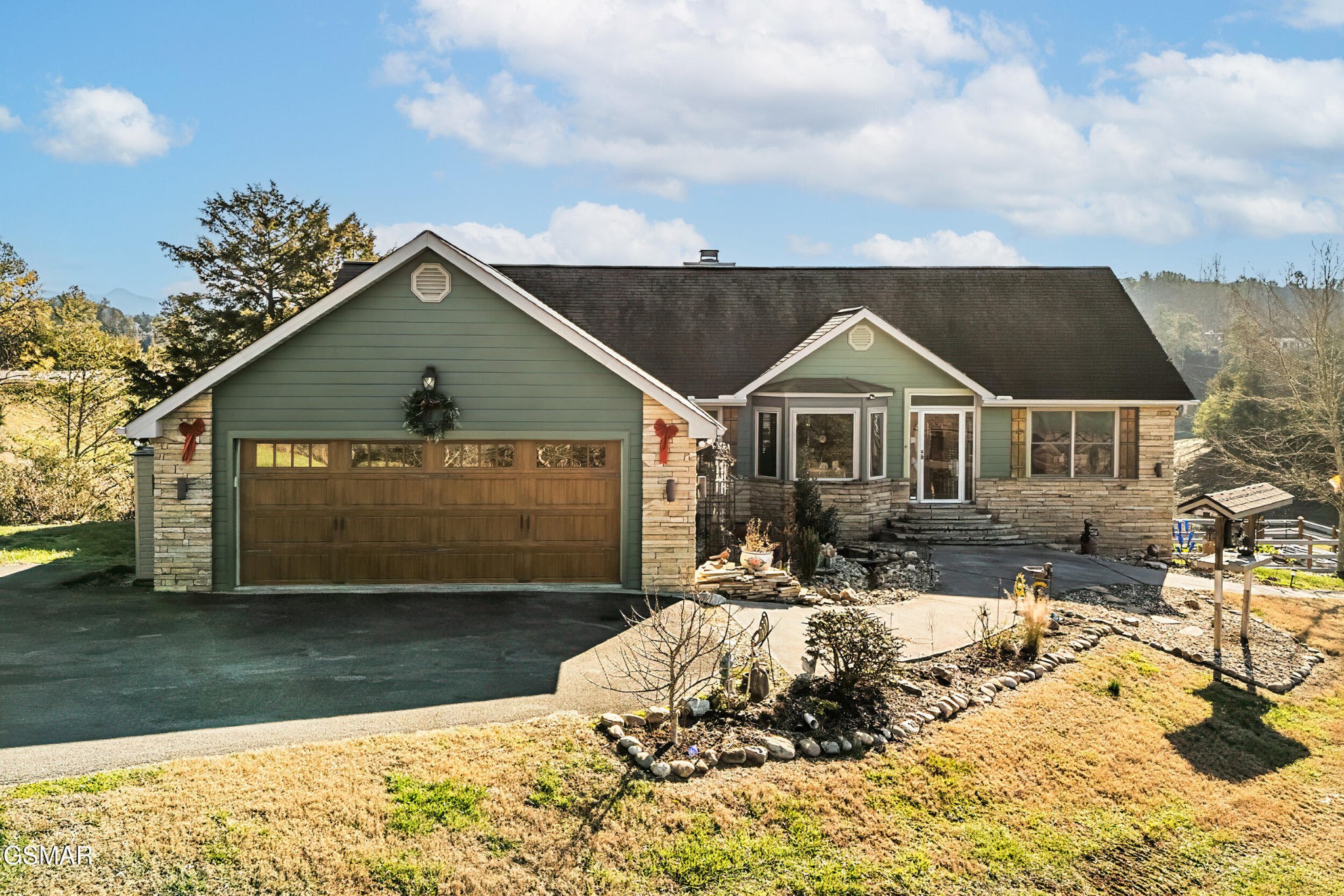 Green and stone house with a wide wooden double garage door and landscaped front yard.