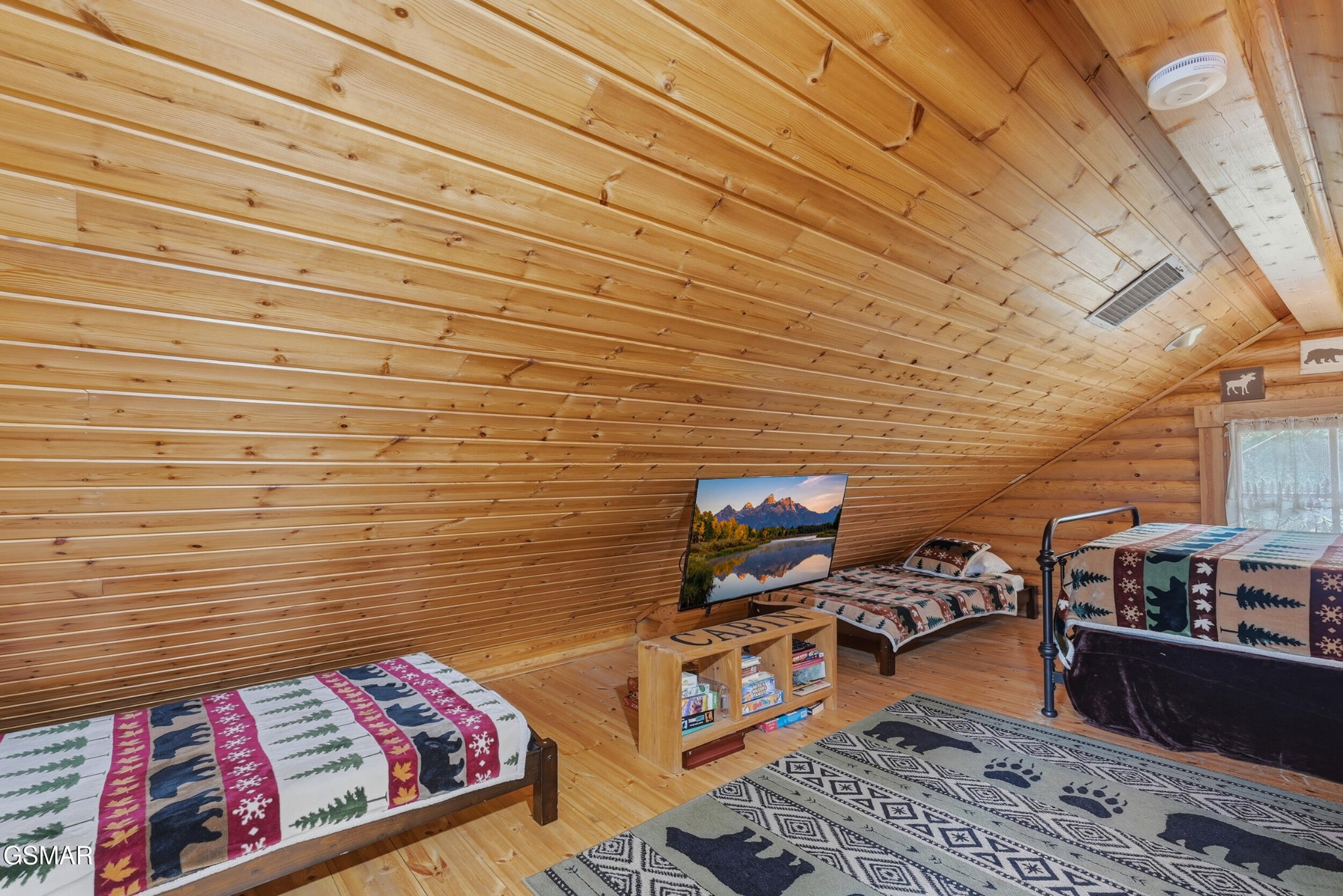 Loft bedroom with three single beds beneath a sloped pine ceiling and bear-patterned rugs.