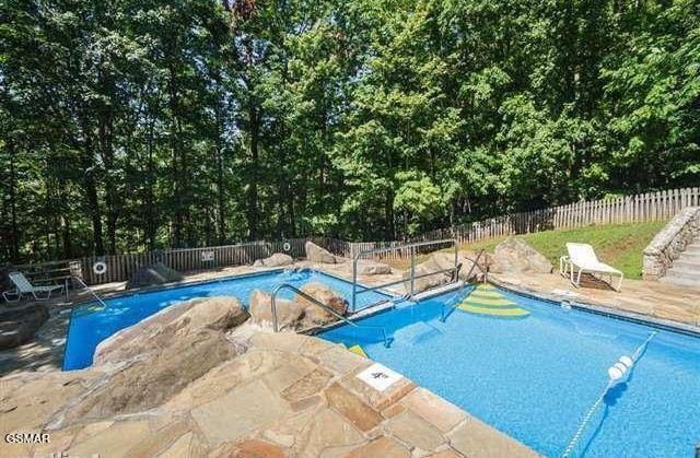 Outdoor pool with a stone patio, decorative rocks, and a wooded fenced setting.
