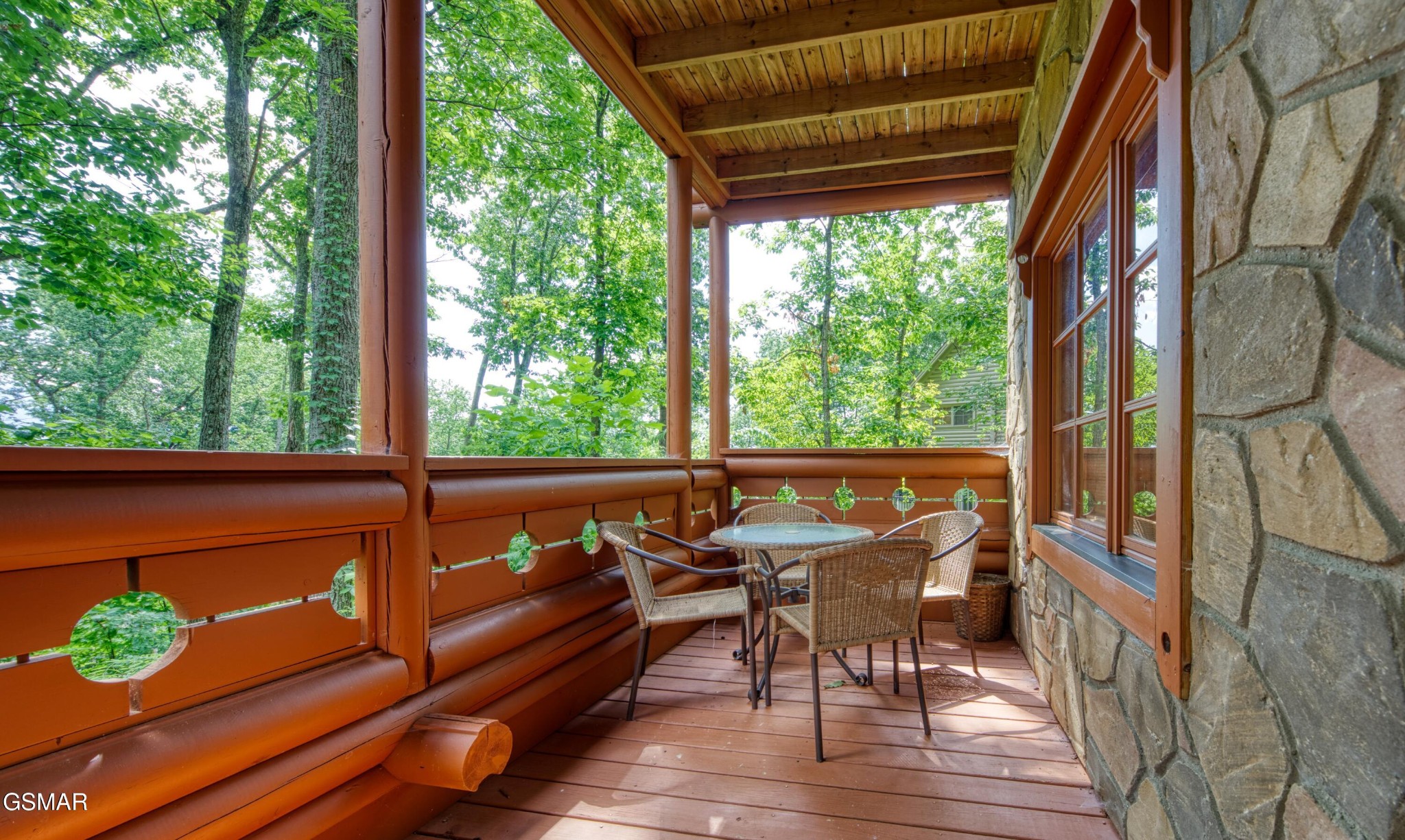 Covered wooden porch with wicker seating and a leafy woodland view.