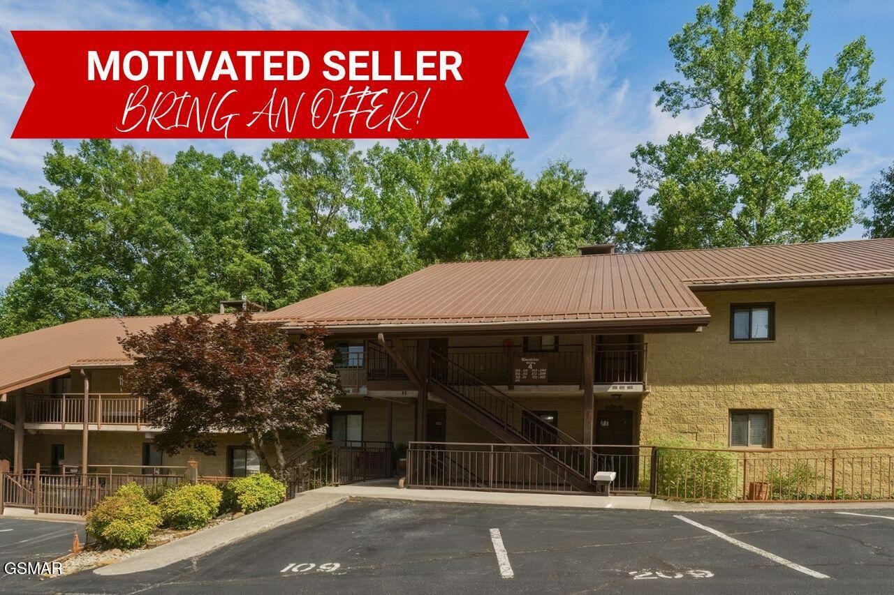 Two-story tan residential building with a brown metal roof, exterior stairs, balconies, and front parking lot.