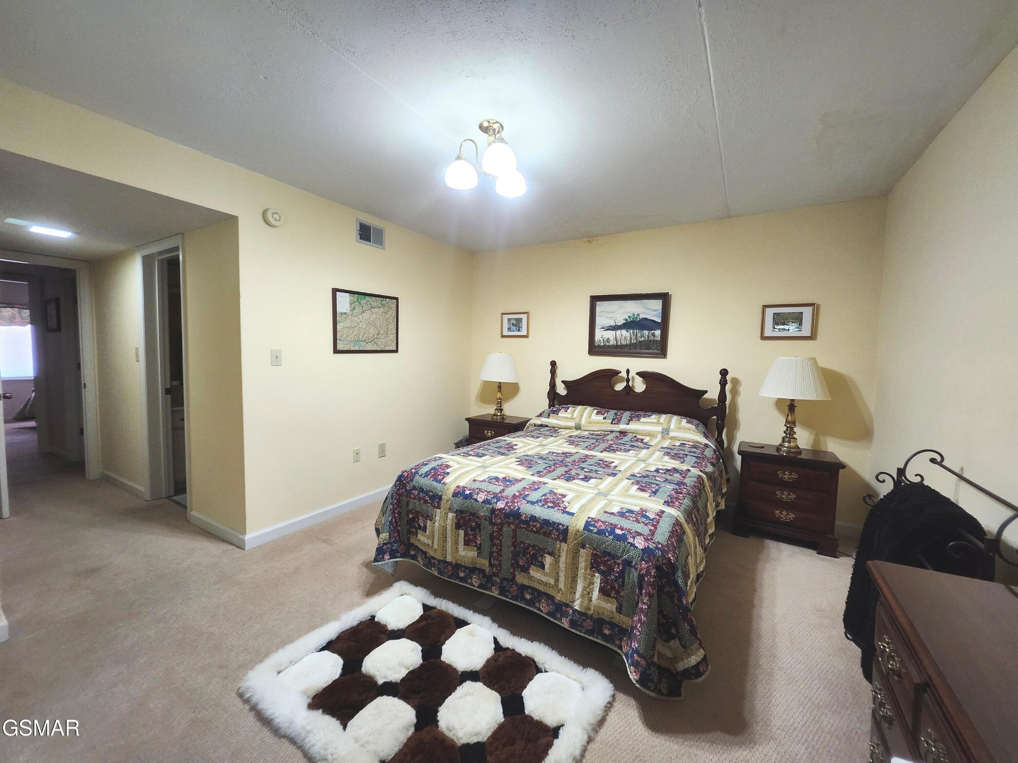 Bedroom with a patchwork quilt, matching bedside tables, and a brown-and-white rug.