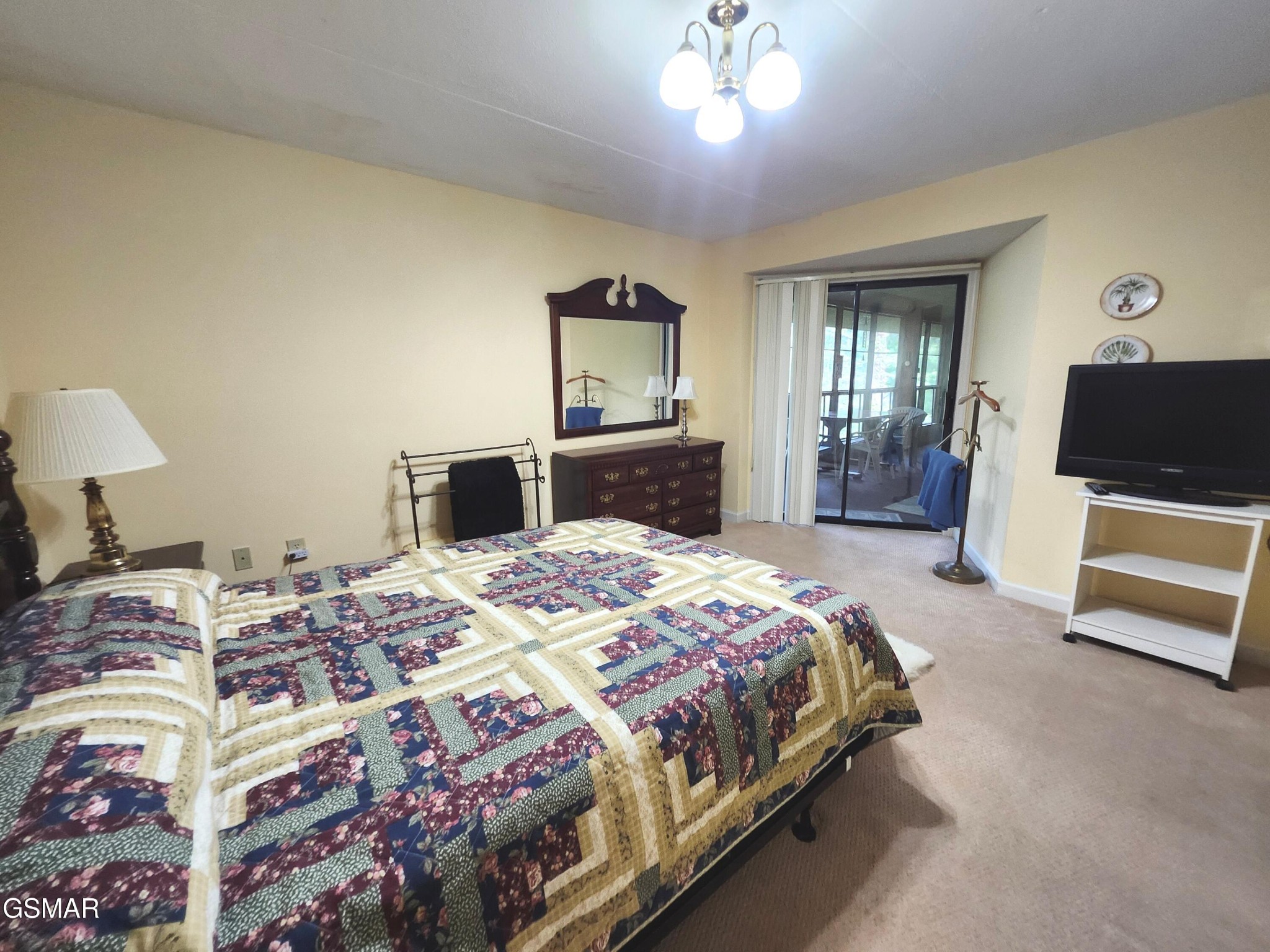 Furnished bedroom with a patchwork quilt, dark wood dresser, and sliding doors to a balcony.