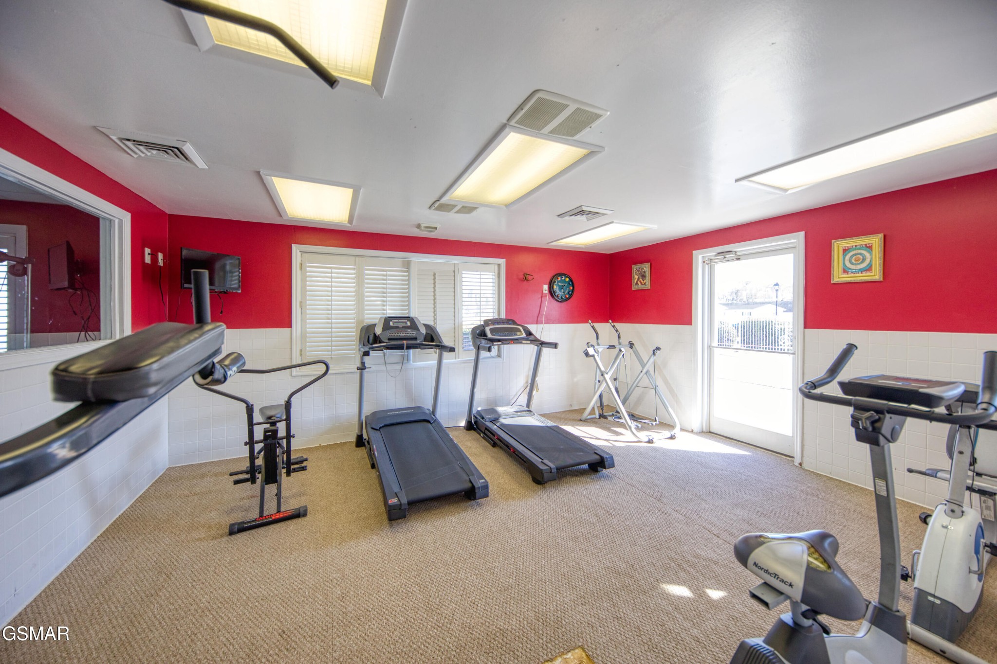 Home gym with treadmills and exercise bikes, red walls, and a glass door.