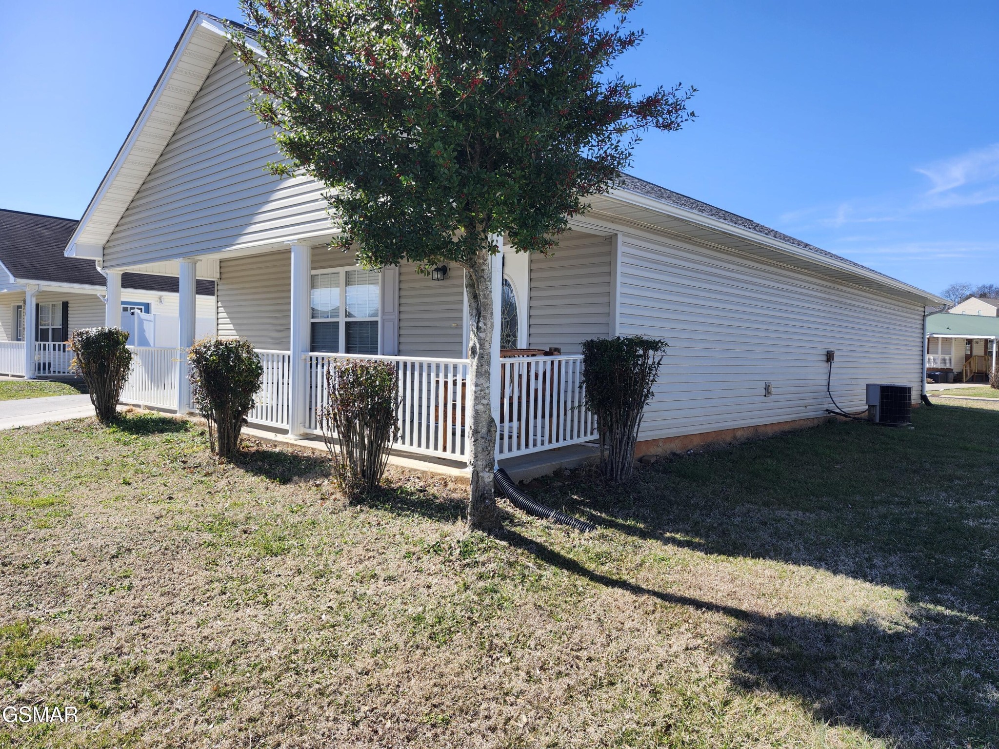 Single-story home with a covered white-railed porch, partly screened by a mature tree.