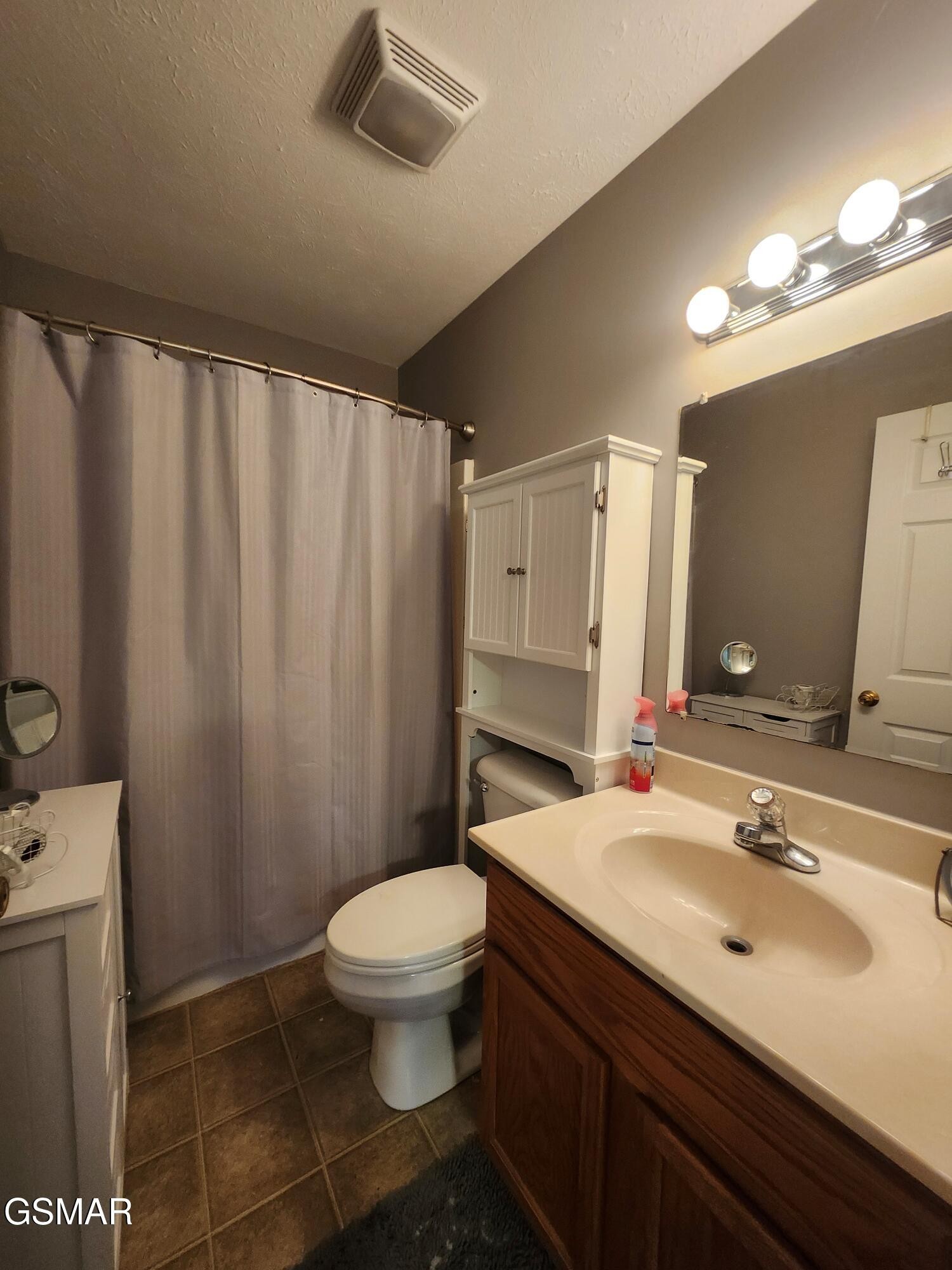 Bathroom with a dark wood vanity, white sink, curtained shower, and wall cabinet.