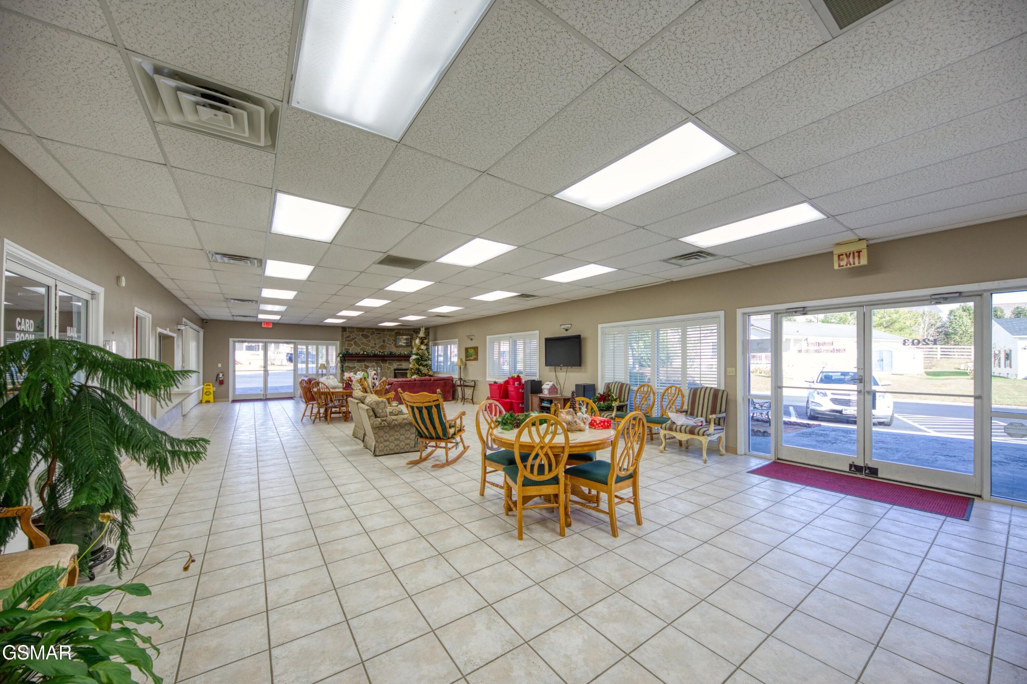 Furnished communal lounge with tiled floors, seating areas, dining tables, and glass doors.