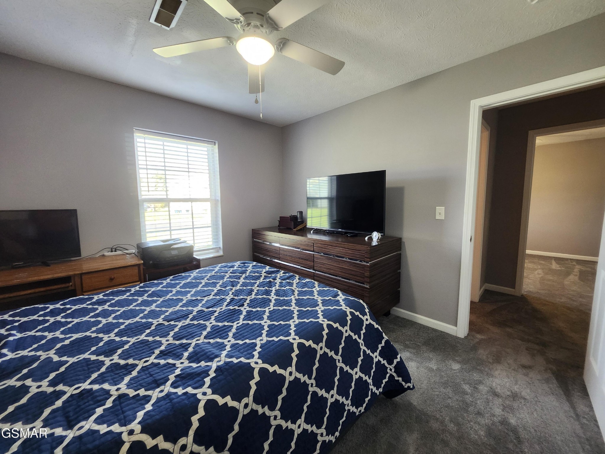 Bedroom with a navy-and-white patterned bedspread, window blinds, and televisions.