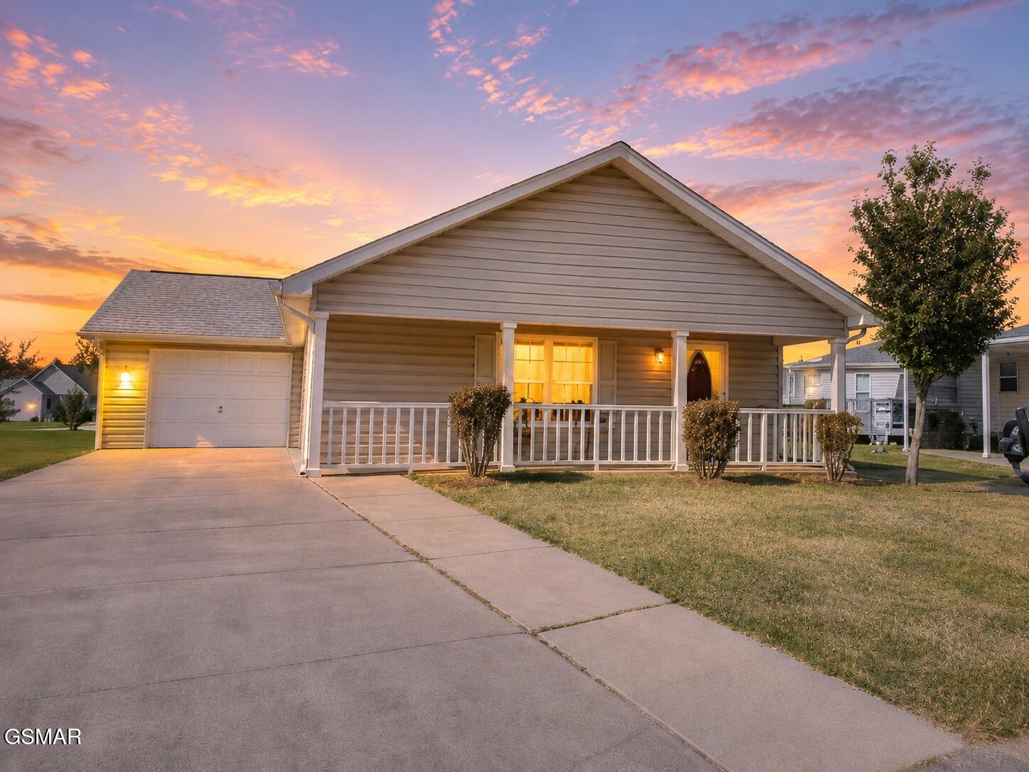 Single-story home with a covered porch and attached garage beneath a colorful dusk sky.