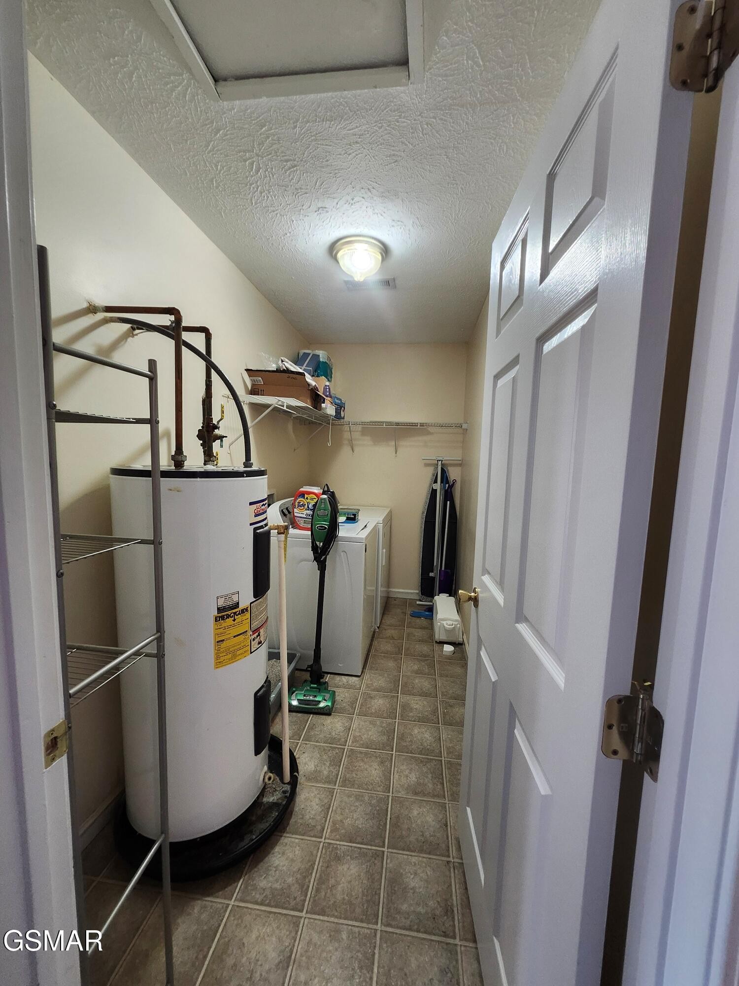 Laundry room with a large water heater, washer, and tiled floor.